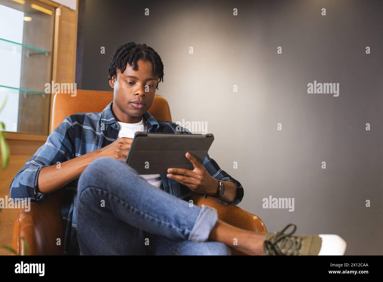 Uomo afroamericano seduto in un moderno ufficio aziendale, che usa un tablet con spazio per le copie. Ha i capelli neri corti, indossa abiti casual, inalterati Foto Stock