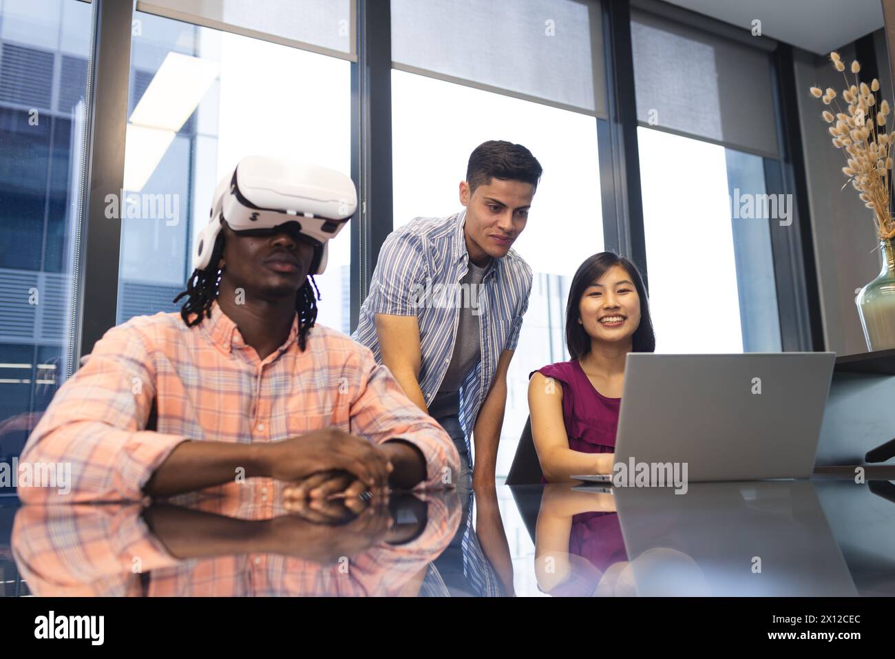 Gruppi diversi di colleghi che esplorano la realtà virtuale e utilizzano un notebook in un moderno ufficio aziendale Foto Stock