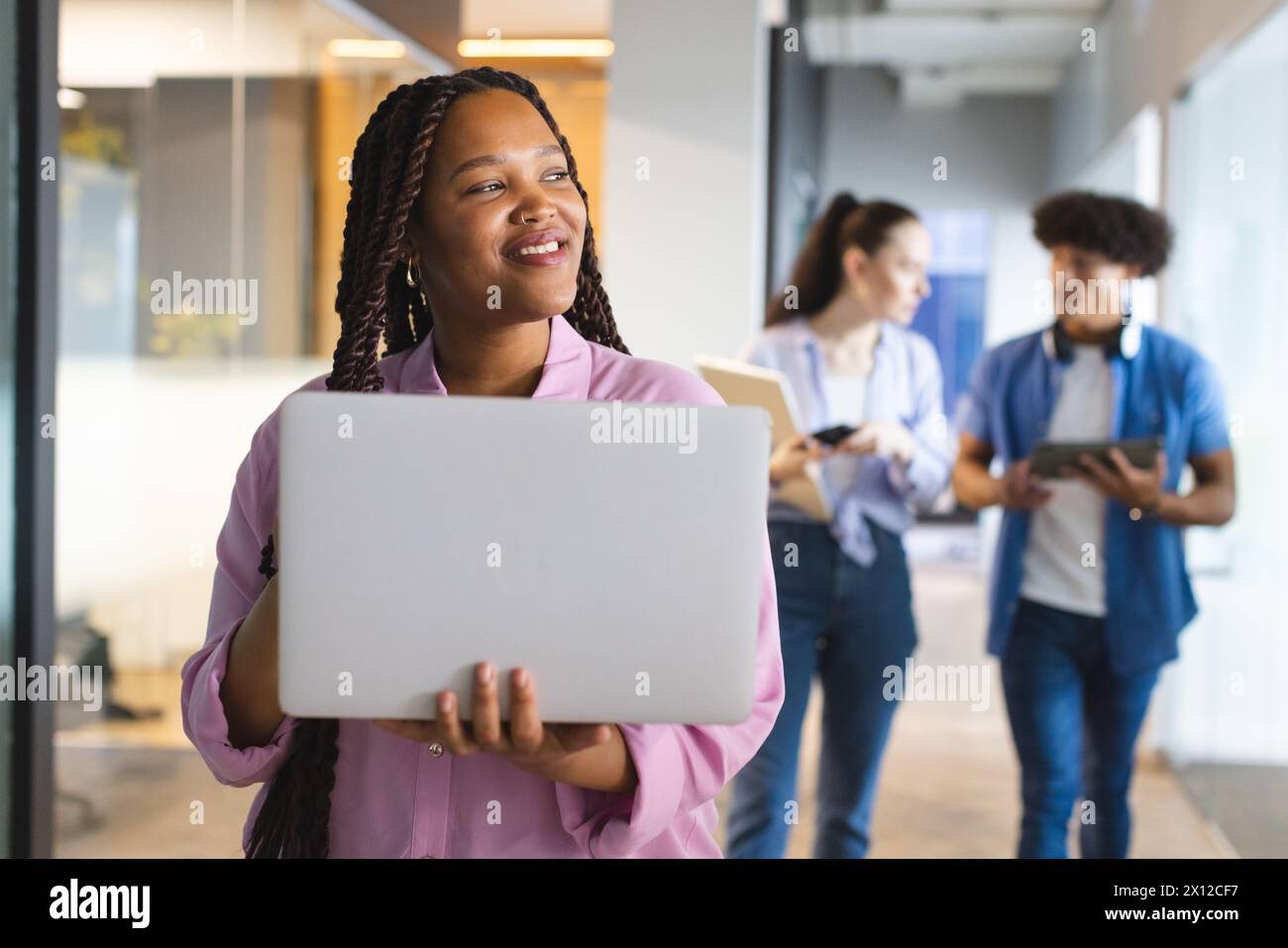 Una giovane donna birazziale che tiene in mano un notebook, colleghi che chiacchierano in un moderno ufficio aziendale Foto Stock