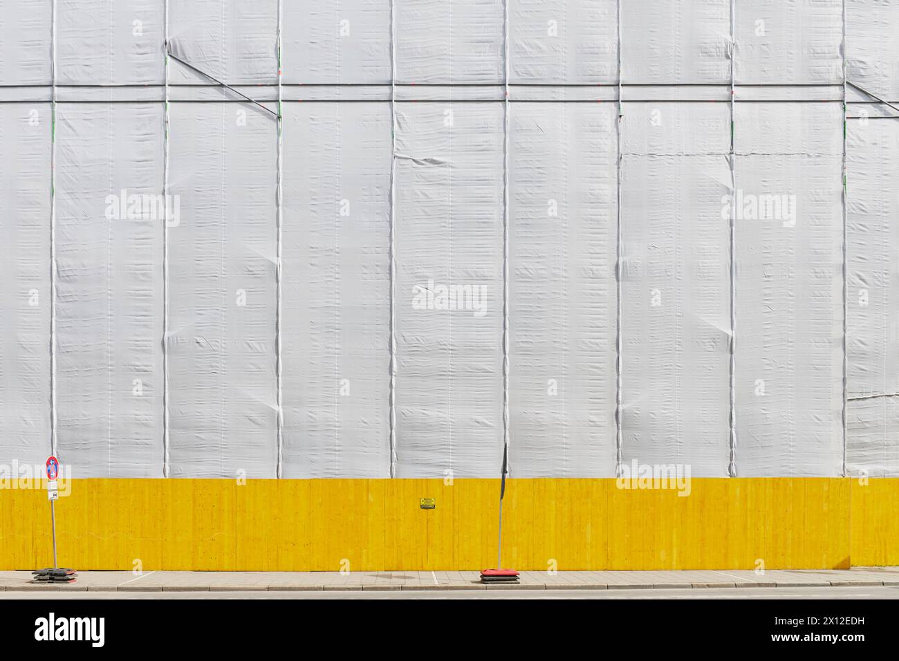 Wegen Bauarbeiten abgehängte Fassade mit gelbem Bauzaun im hellen Sonnenschein Foto Stock