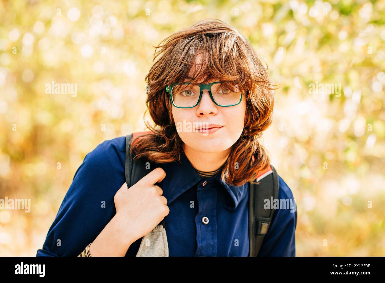 Studentessa universitaria con occhiali verdi e zaino che cammina nel parco Foto Stock
