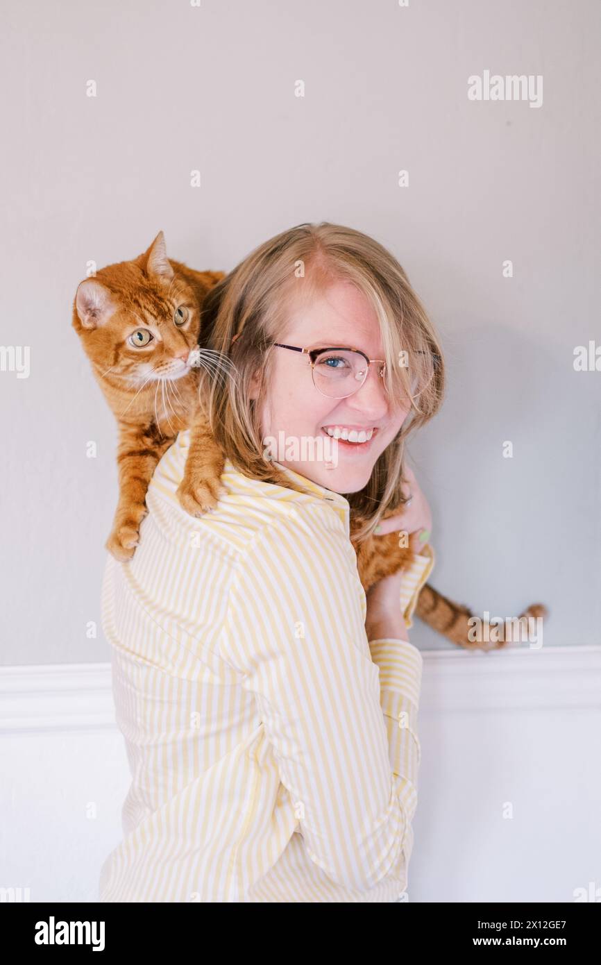 Donna gioiosa con gatto di zenzero a spalla in interni Foto Stock
