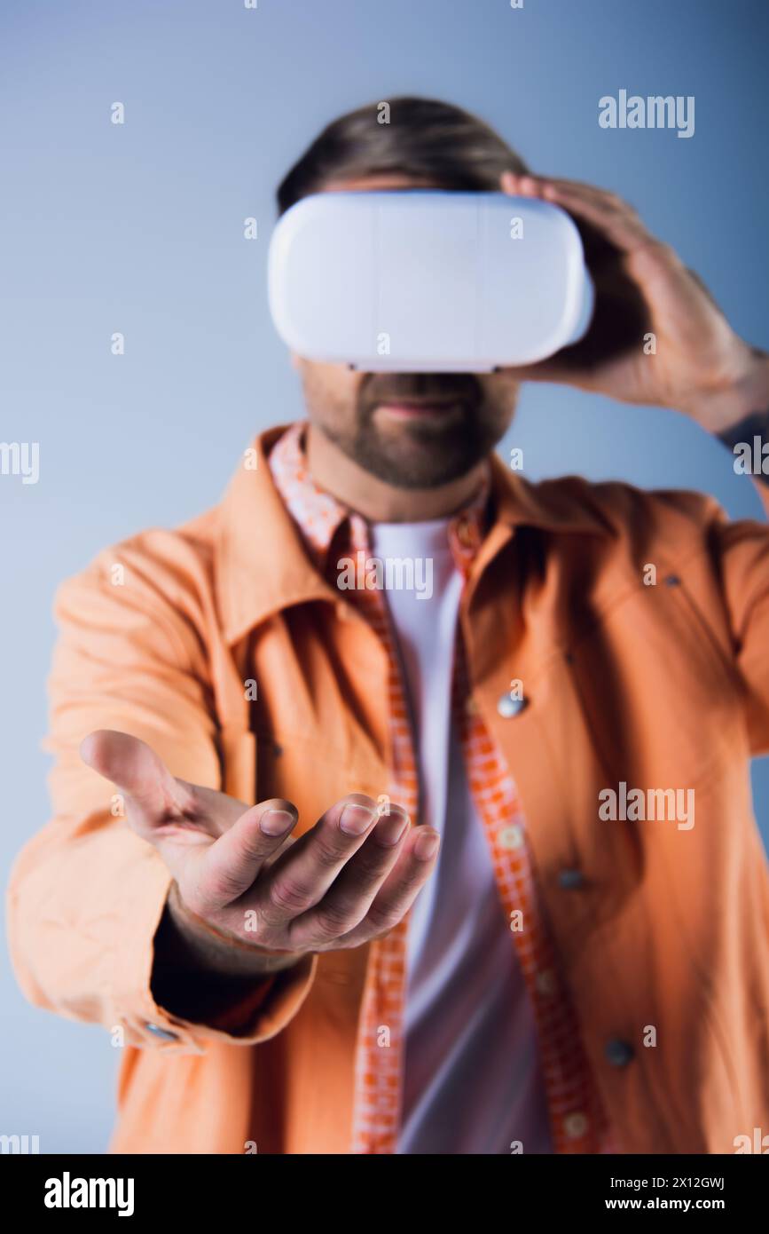 Un uomo con una camicia arancione regge un oggetto bianco in uno studio, emettendo un'aura di mistero e meraviglia. Foto Stock