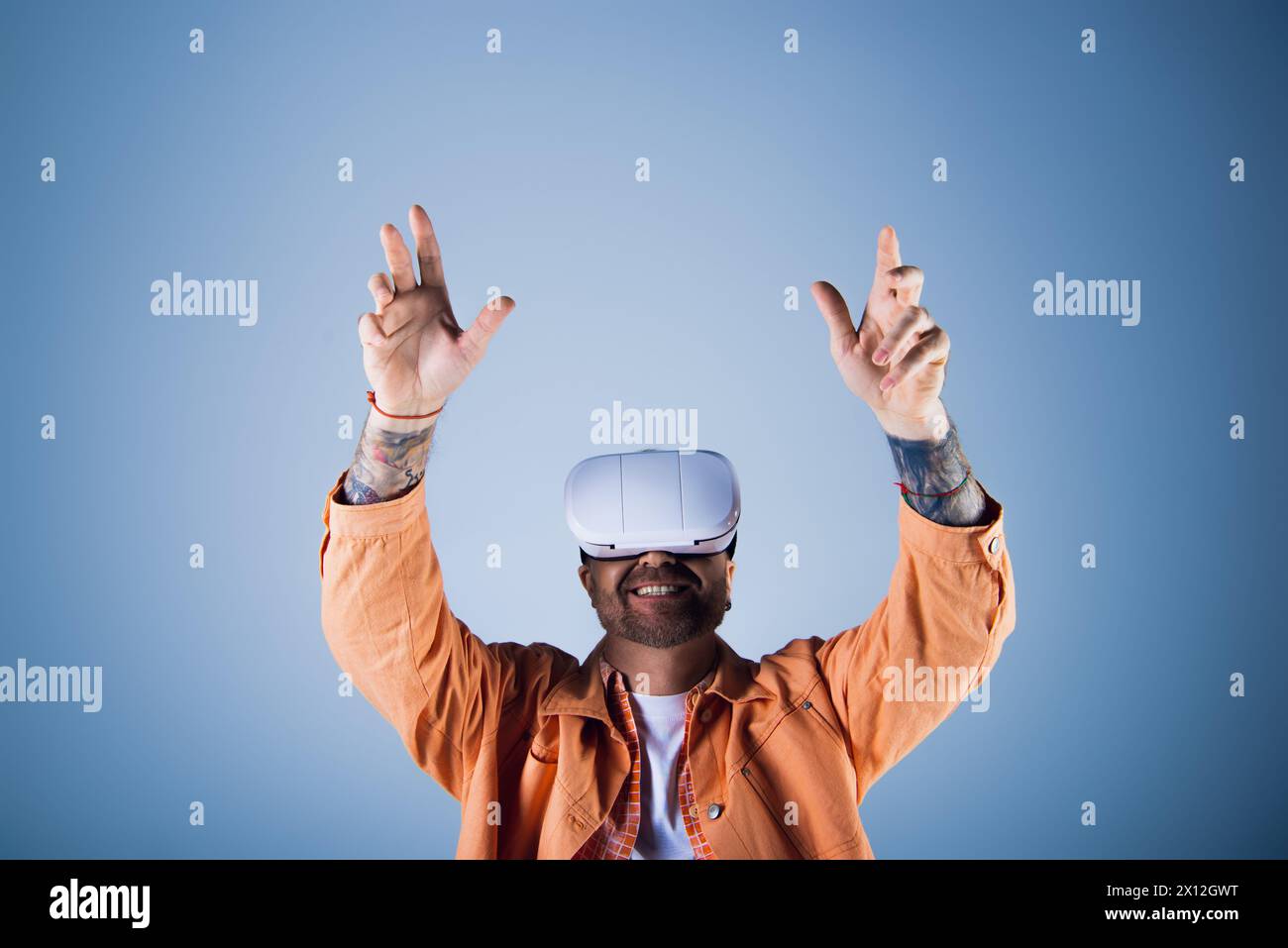 Un uomo con una giacca arancione indossa un visore vr bianco su uno sfondo vivace. Foto Stock