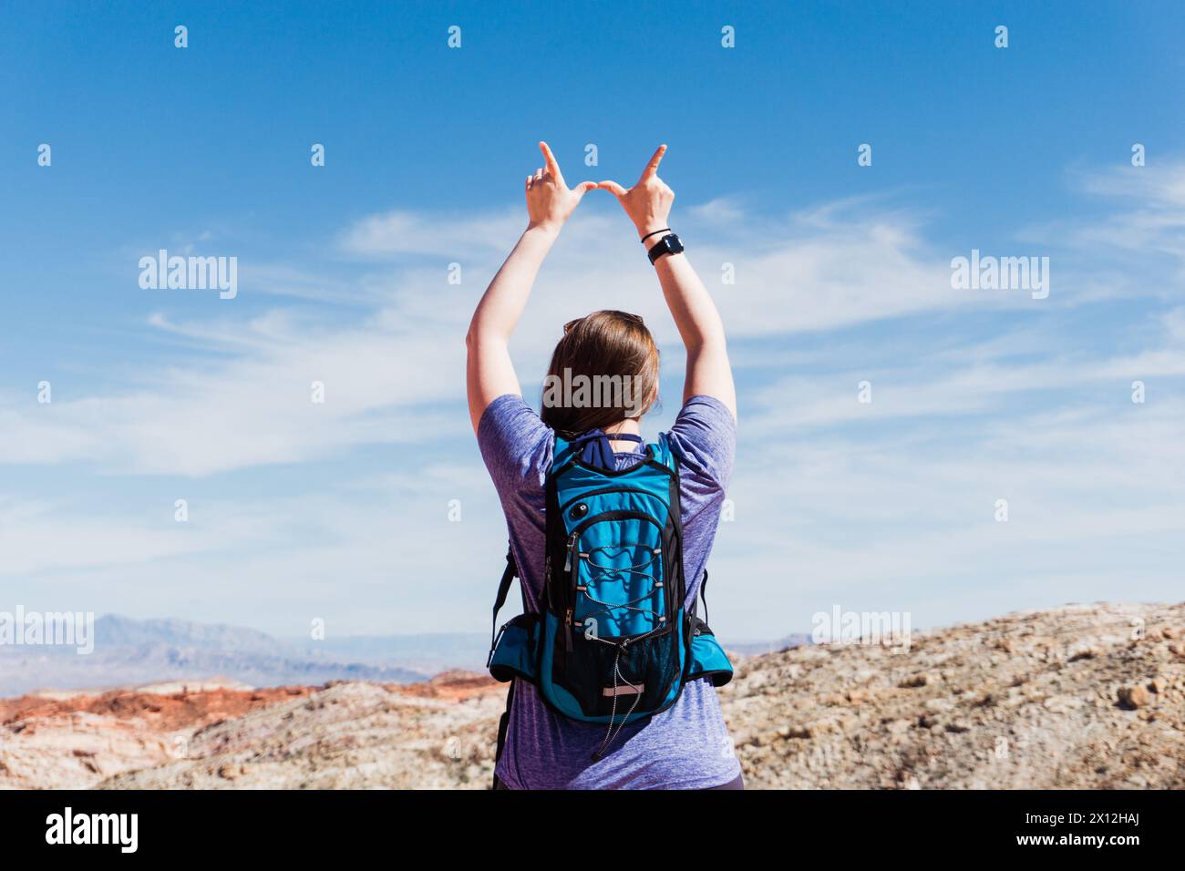 L'escursionista con una camicia viola crea un cartello con la "W" sotto il cielo del deserto Foto Stock
