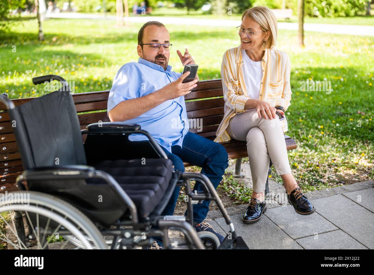 L'uomo in sedia a rotelle sta trascorrendo del tempo con sua madre nel parco. Foto Stock