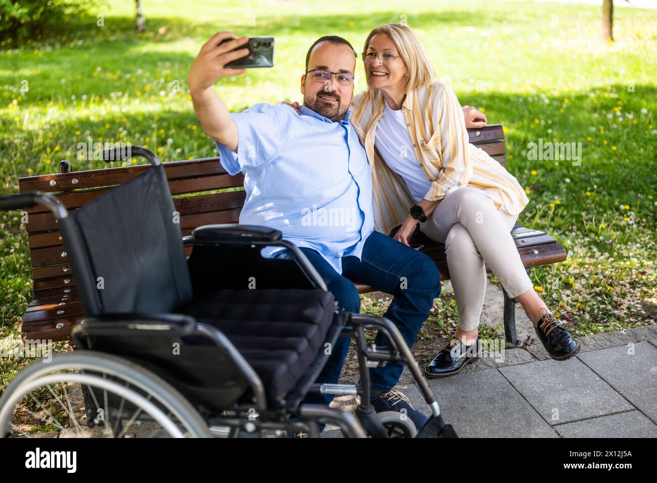 L'uomo in sedia a rotelle sta trascorrendo del tempo con sua madre nel parco. Stanno facendo selfie. Foto Stock
