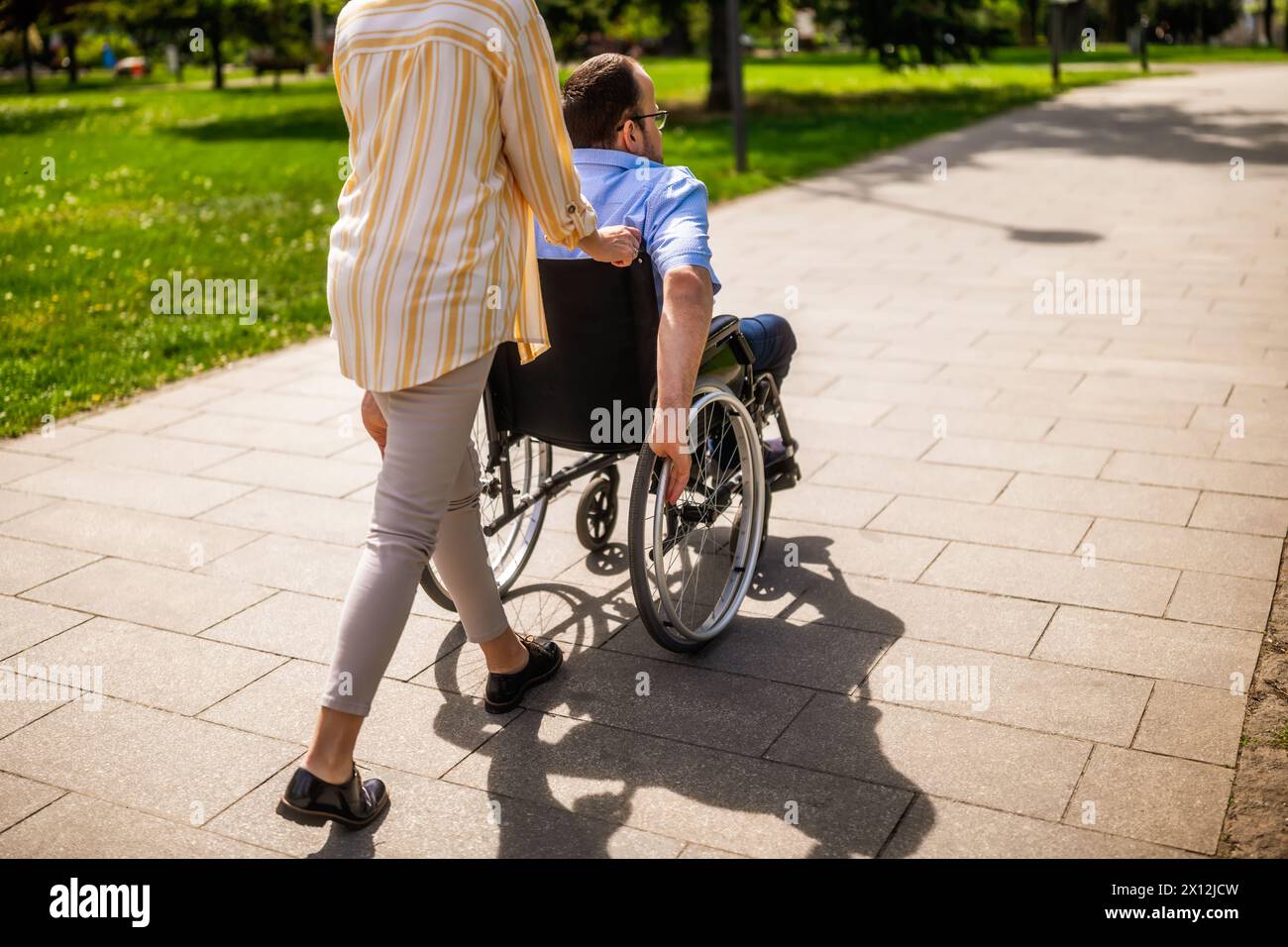 L'uomo in sedia a rotelle sta trascorrendo del tempo con sua madre nel parco. Stanno godendo la giornata di sole insieme. Foto Stock