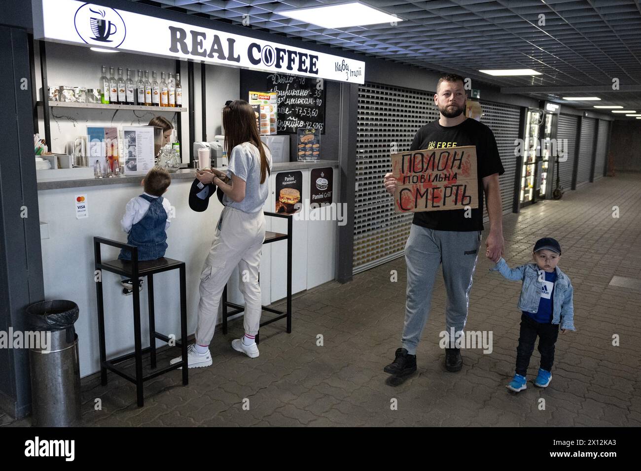 Un uomo ha un cartello con scritto "la prigionia è una morte lenta" mentre cammina davanti a un bar di strada durante una manifestazione nel centro di Kiev. I parenti dei difensori dell'impianto metallurgico Azovstal organizzarono una manifestazione chiedendo alle autorità ucraine di liberare e restituire i loro parenti dalla prigionia russa. (Foto di Oleksii Chumachenko / SOPA Images/Sipa USA) Foto Stock