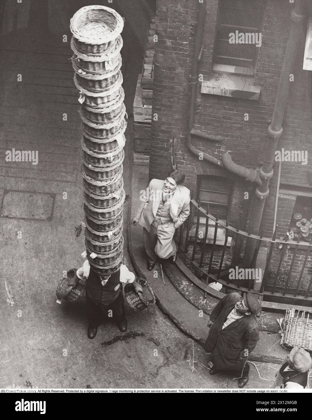Chi ha il maggior numero di cesti in equilibrio sulla testa vince. Il londinese Jimmy Sainsbury ha battuto il record mondiale per il numero di cestini trasportati nel 1932. Covent Garden è sempre stato un ottimo mix di locale e glamour. Fu una delle prime piazze di Londra e si sviluppò come il principale mercato di fiori e verdure di Londra. La piazza è stata progettata da Inigo Jones nel XVII secolo e completata nel 1631 con il mercato ortofrutticolo emergente in questo periodo. Il grande mercato è stato costruito nel 1830 e si trova ancora oggi, anche se la frutta, la verdura e i fiori sono da tempo disappannati Foto Stock