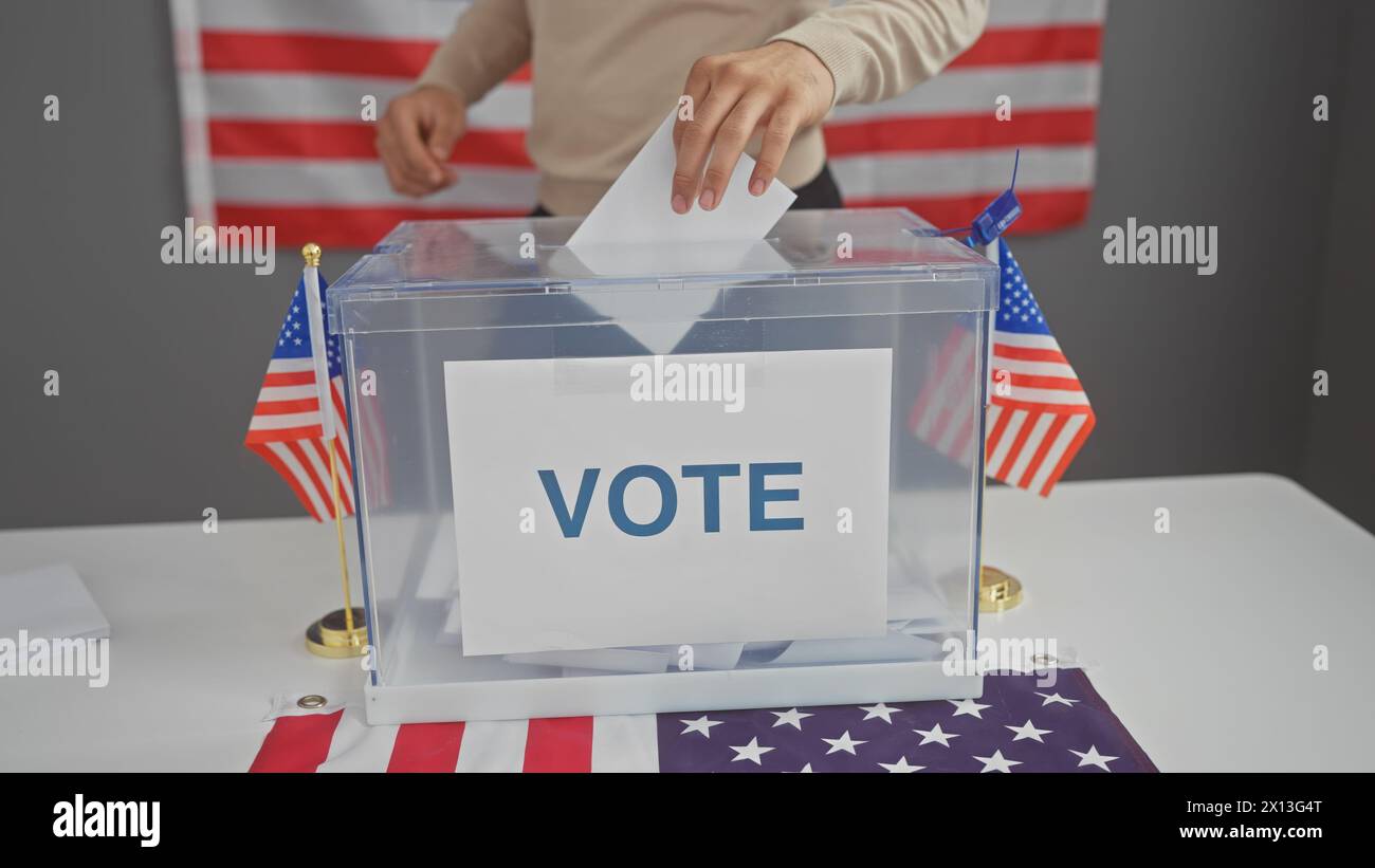 Cittadino che ha lanciato un voto in un centro elettorale al chiuso degli Stati Uniti, con bandiere americane sullo sfondo. Foto Stock