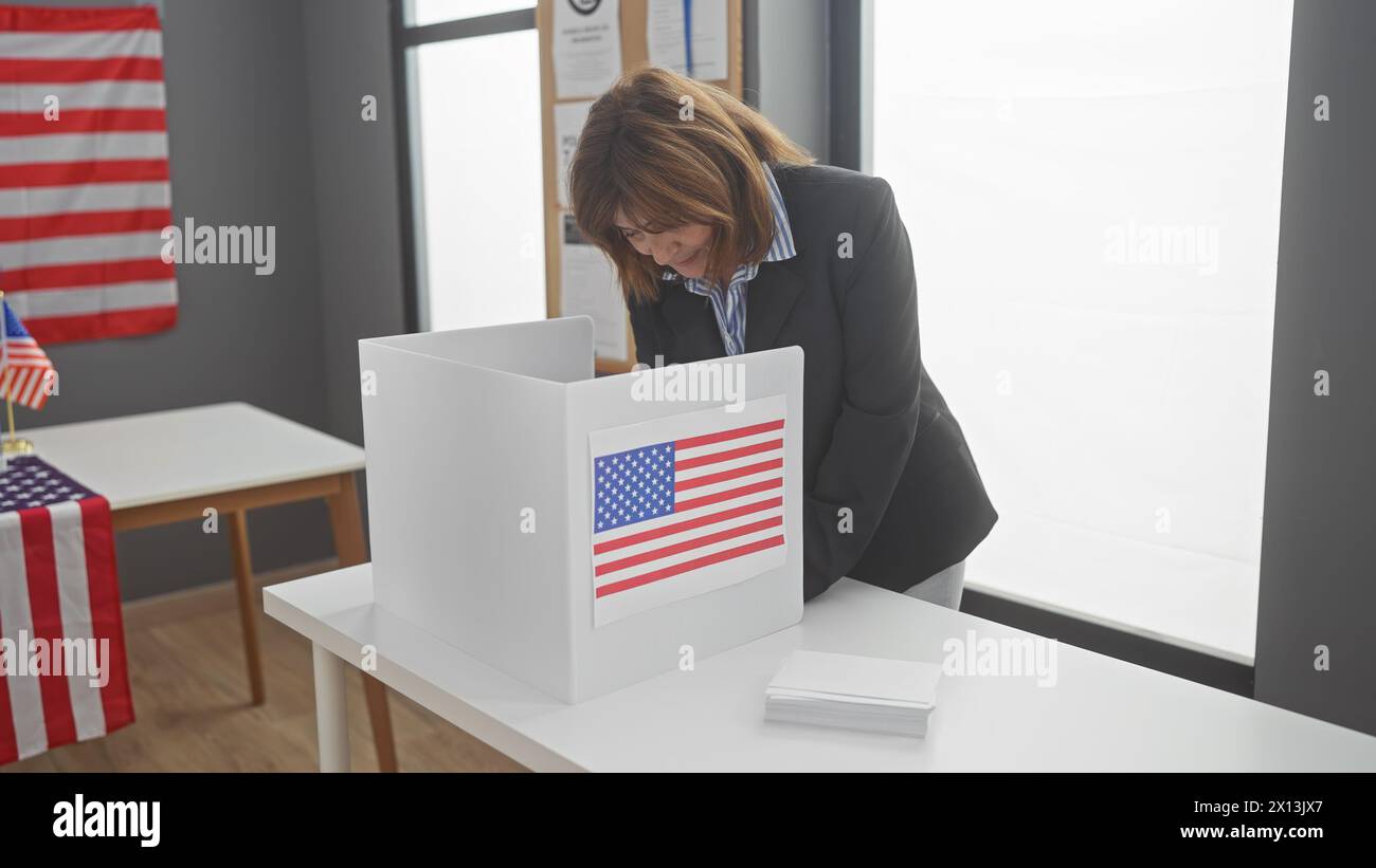 Donna matura che vota nel centro elettorale americano con la bandiera. Foto Stock