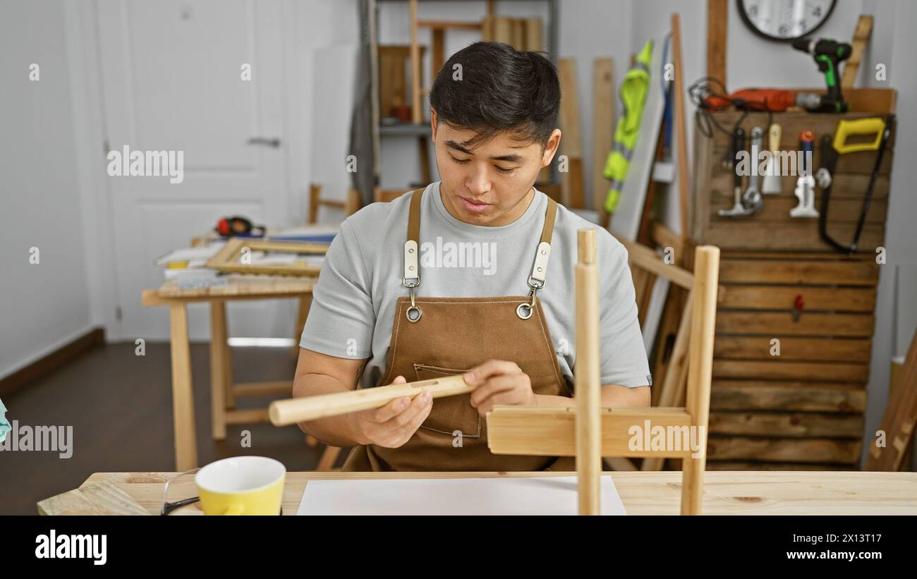 Un uomo asiatico specializzato nella levigatura del legno in un laboratorio di falegnameria ben organizzato Foto Stock