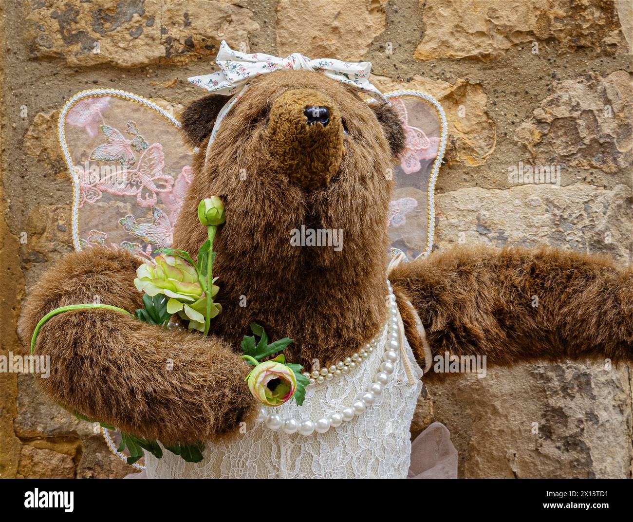 Un grande orso marrone tenero che indossa un abito con ali d'angelo e un collo senza perle. Incontri, matrimonio, uscire, genere o concetto di identità Foto Stock