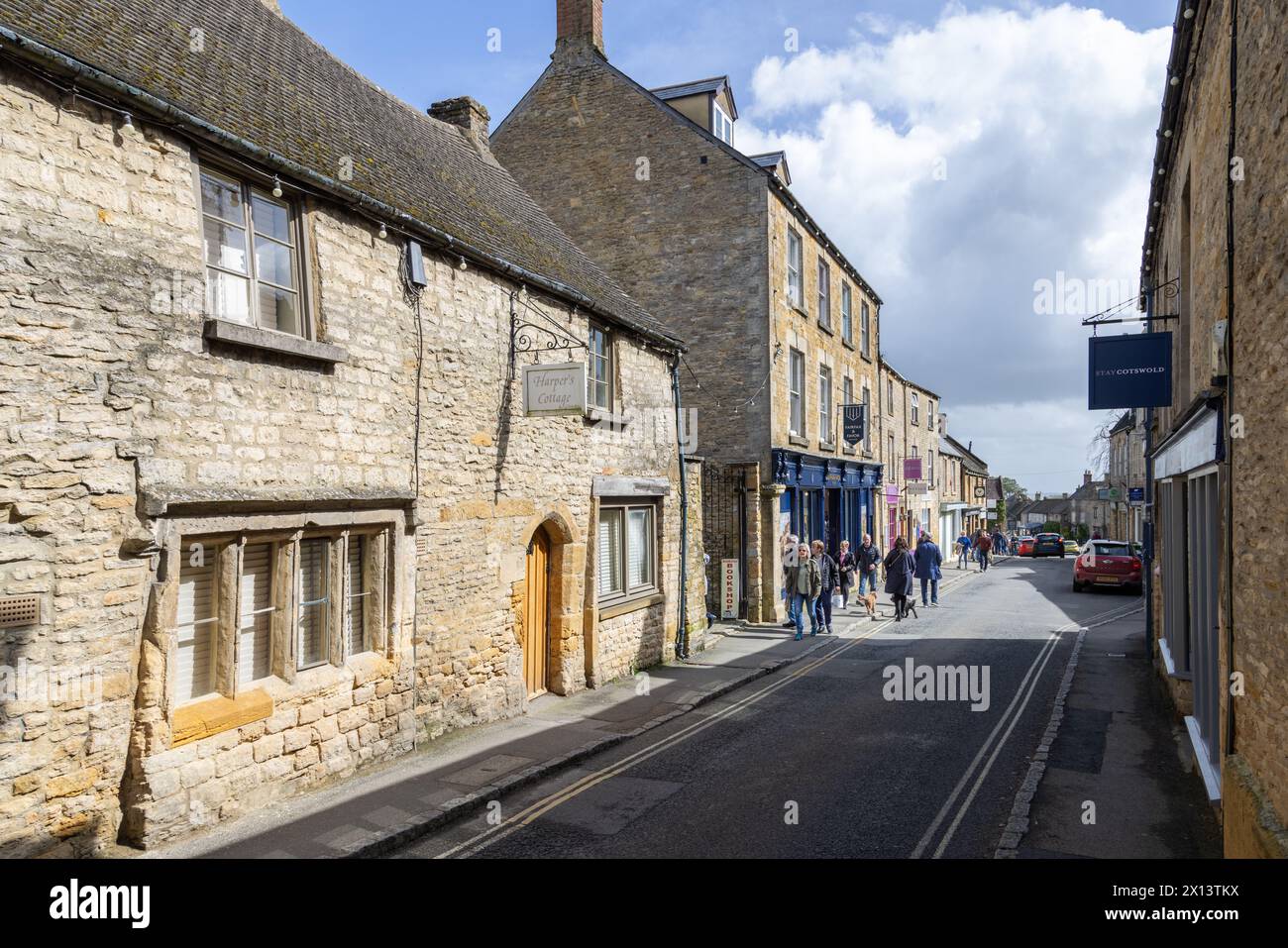 I turisti e gli amanti dello shopping passeggiano lungo una strada costeggiata da negozi di pietra del Cotswold color miele a Stow on the Wold. La popolare destinazione delle Cotswolds. Foto Stock