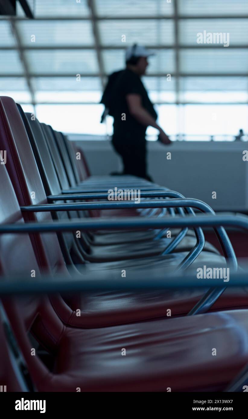 Un passeggero attraversa un terminal dell'aeroporto e passa davanti a file sfocate di sedie vuote mentre si dirige al gate d'imbarco per il suo volo a Parigi Foto Stock