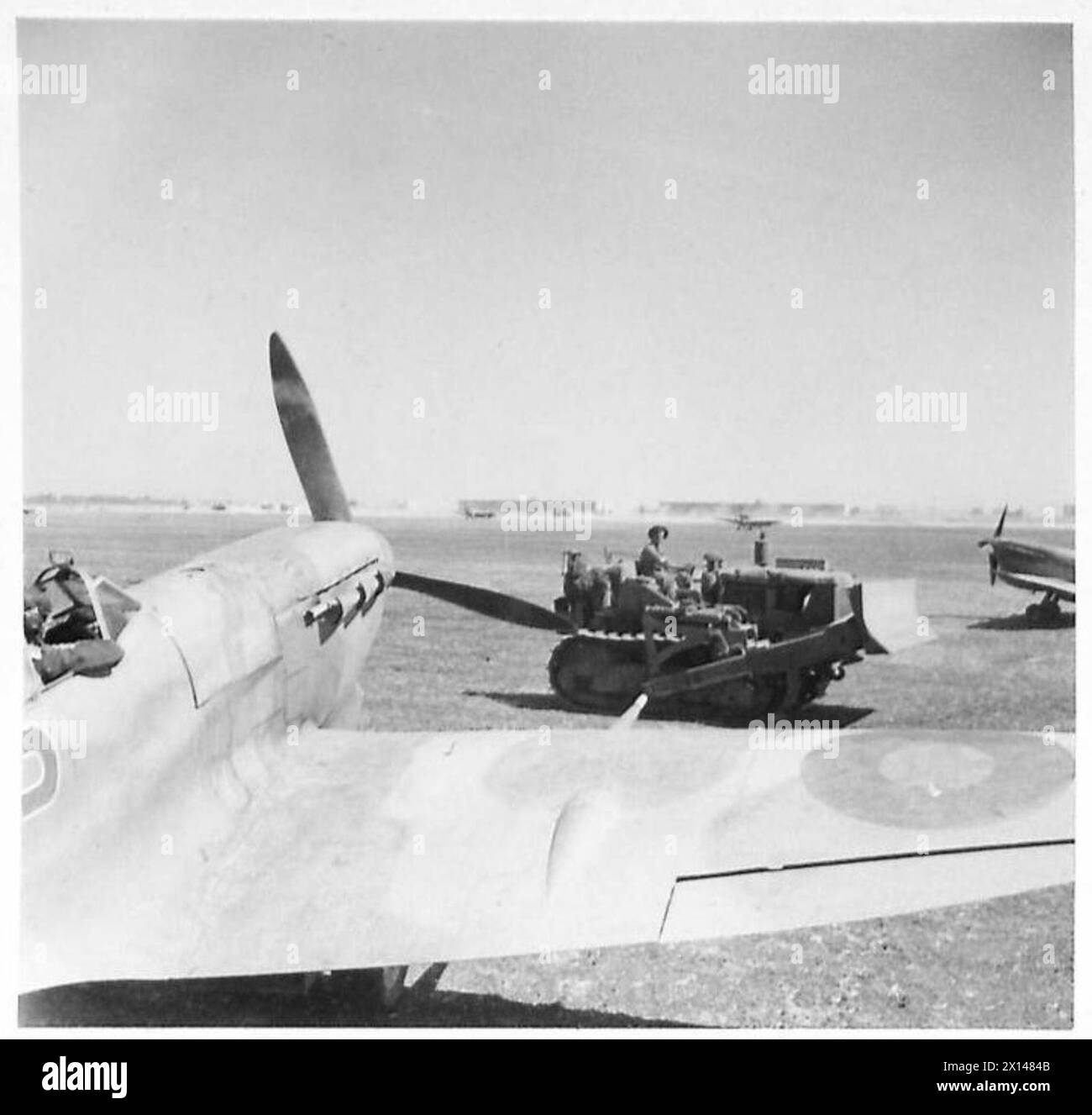 Un pilota attende di decollare mentre osserva un bulldozer che livella un campo durante i preparativi per l'invasione della Sicilia da parte dell'esercito britannico. Foto Stock