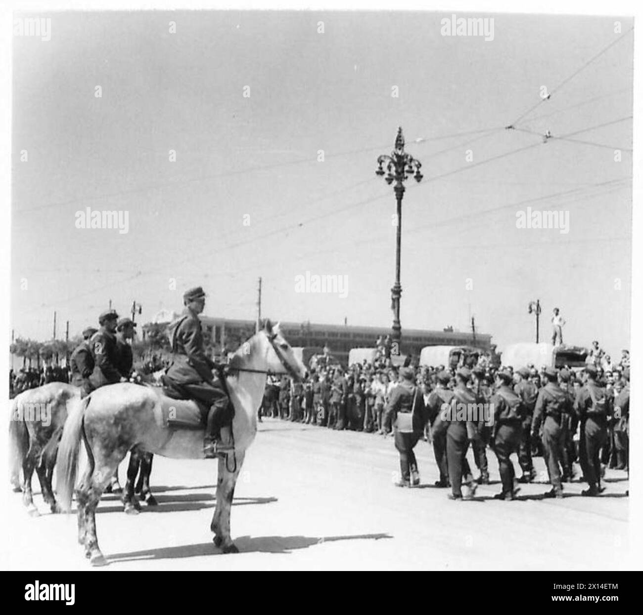 Le truppe dell'Ottava Armata marciano oltre una base salutista nella liberata Trieste, con una pattuglia a cavallo in primo piano. Foto Stock