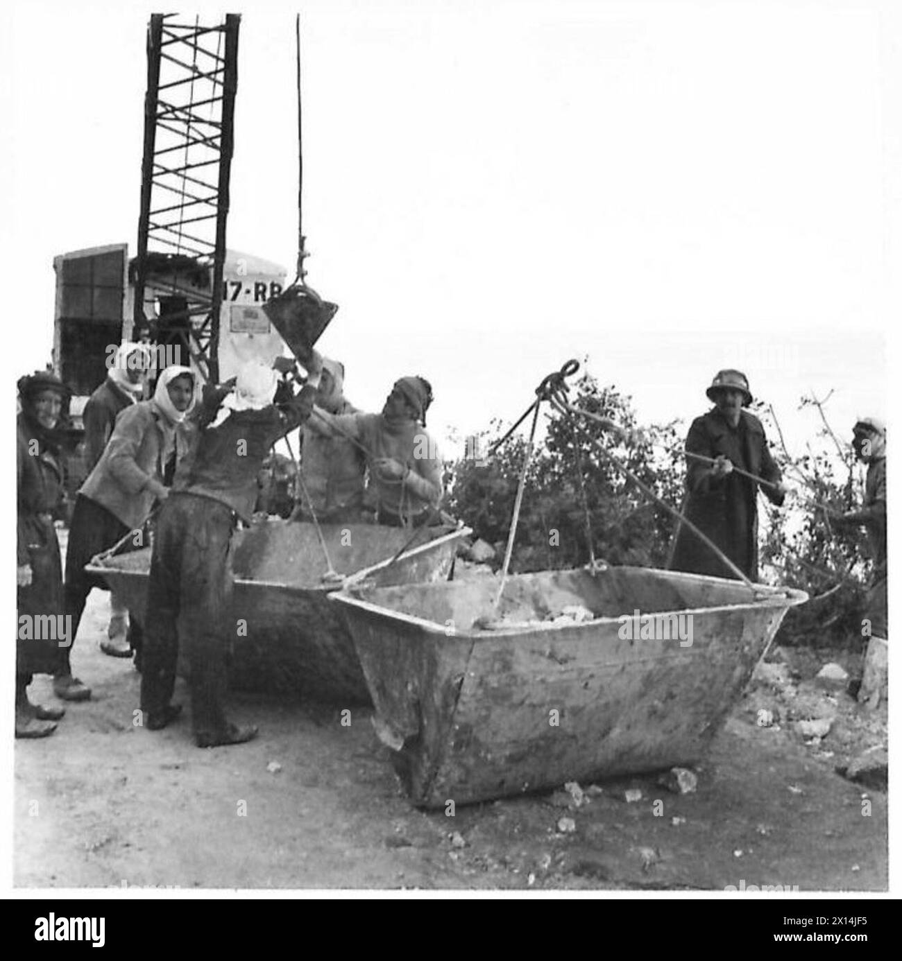 I lavoratori locali caricano secchi per gru con pietre che sono ribaltate verso una mensola su una scogliera dove è in corso la costruzione di un muro per la ferrovia Haifa-Tripoli. Foto Stock