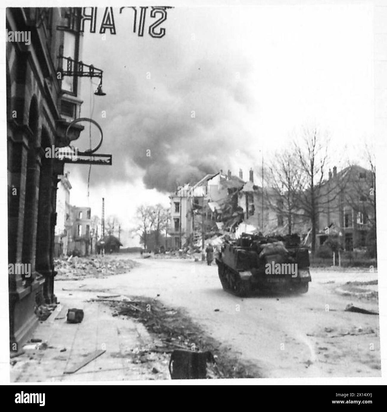 Truppe e veicoli dell'esercito britannico che si muovono per le strade di Arnhem durante il combattimento urbano, con edifici in fiamme, come parte delle operazioni della seconda guerra mondiale da parte del 21st Army Group. Foto Stock