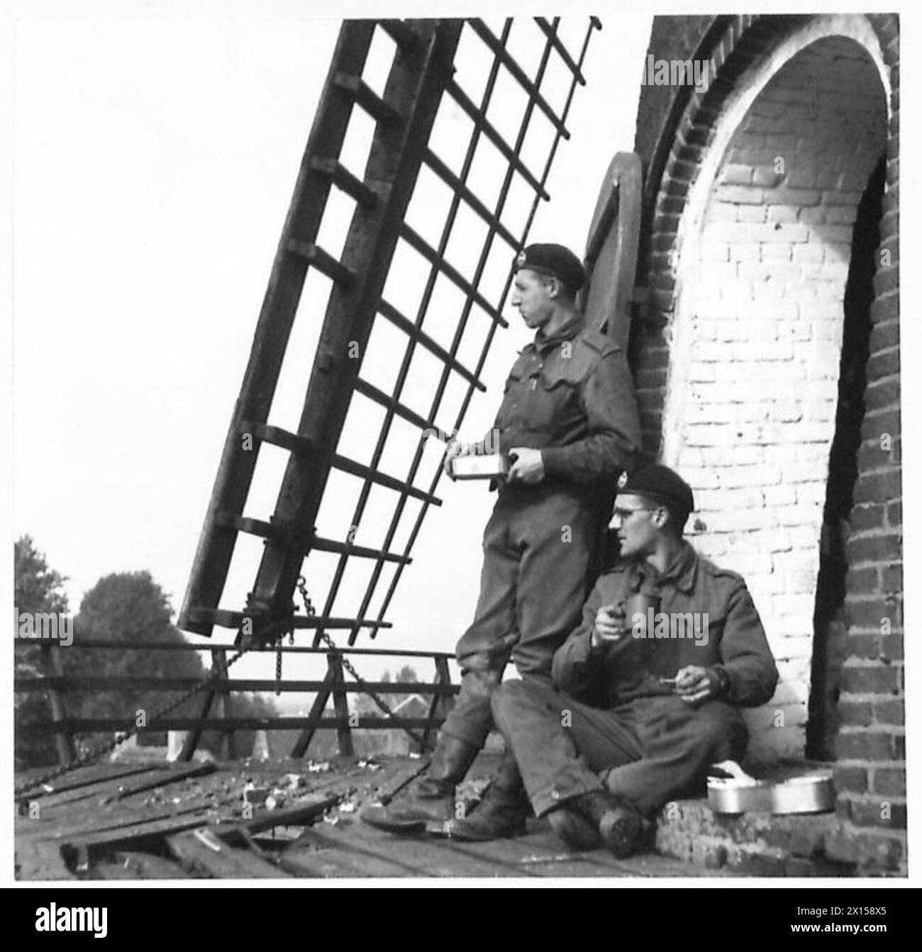 I soldati si riuniscono intorno a un mulino a vento olandese per pranzo, tra cui TPR Leslie Cope e TPR John Chapman, British Army, 21st Army Group. Foto Stock