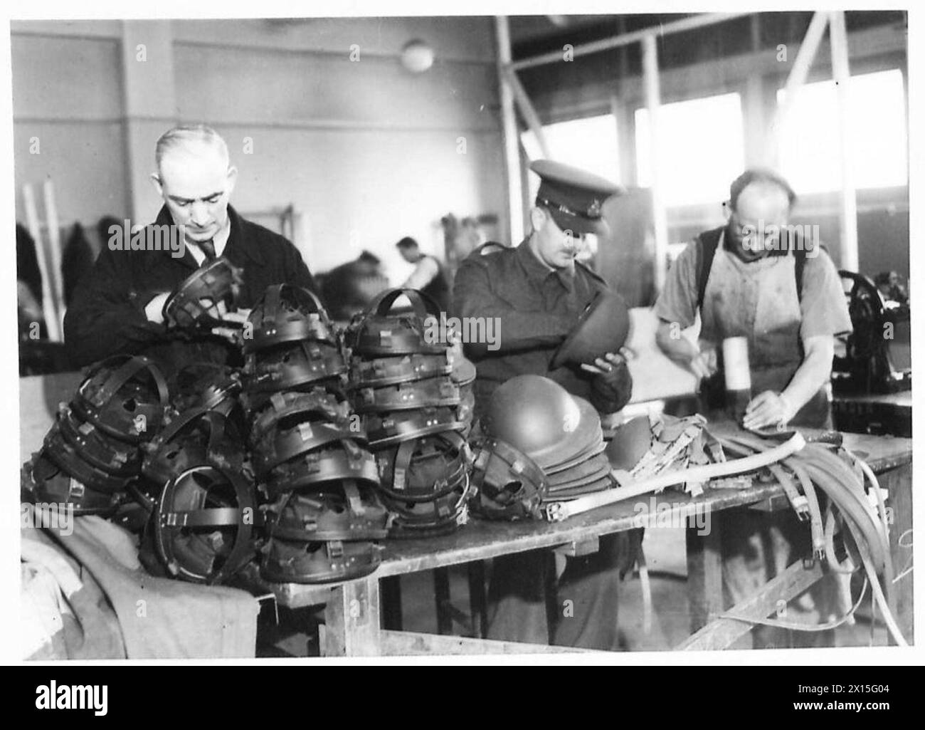Un soldato e civili assemblano caschi d'acciaio, riparando l'equipaggiamento dell'esercito britannico durante le operazioni di guerra. Foto Stock