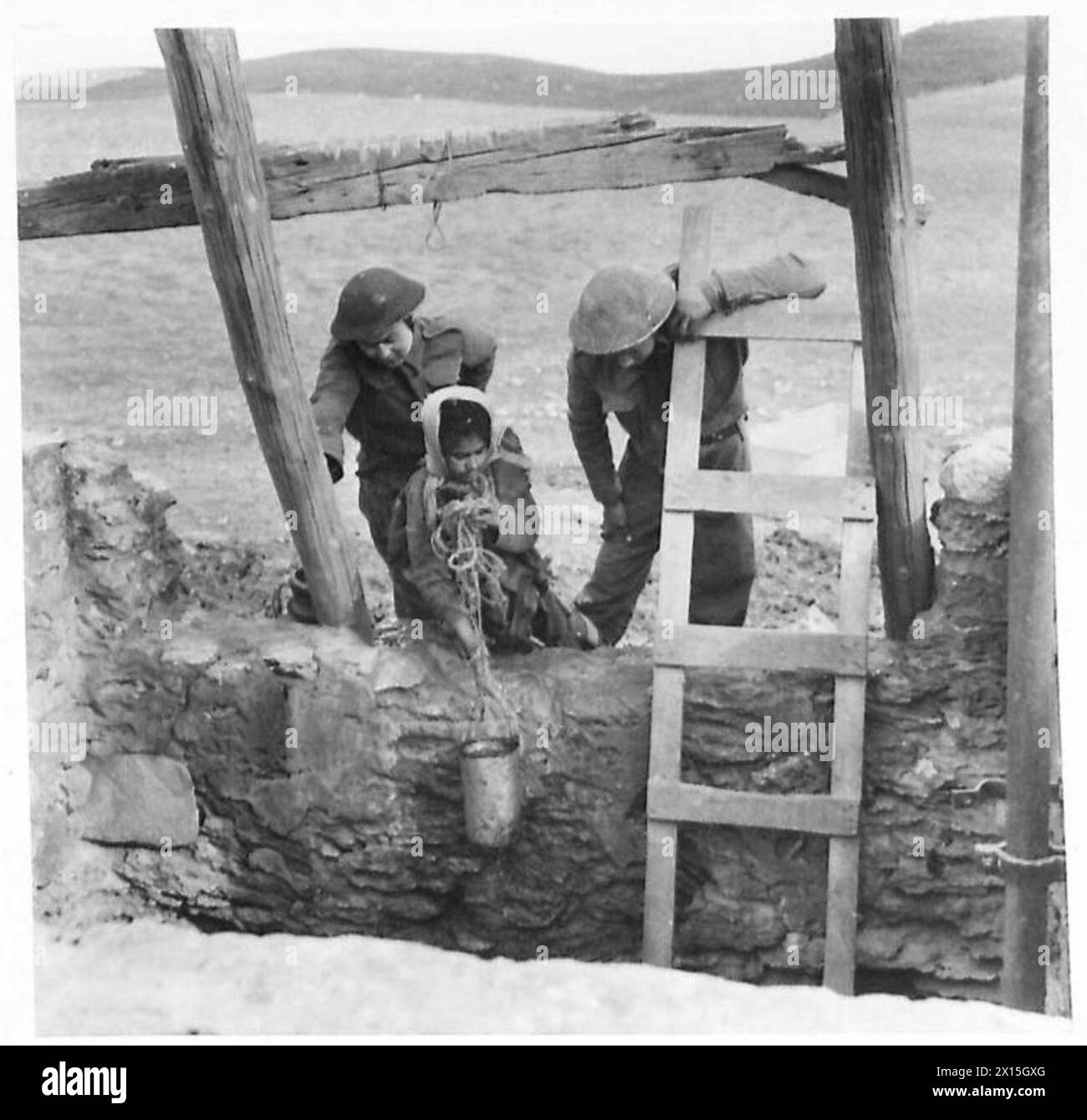 Due cannoni della 255th Battery, Royal Artillery osservano una donna araba che aspira acqua da un pozzo vicino alla loro posizione anticarro da sei libbre sulle colline vicino a Medjez el Bab il 31 dicembre 1942 durante la campagna di Tunisia. Foto Stock