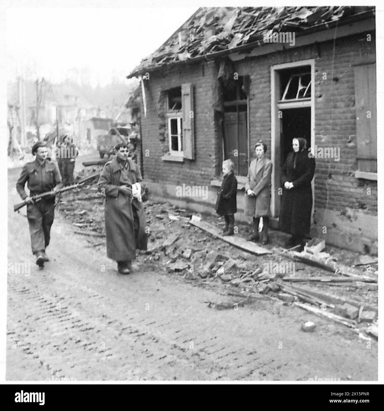 I civili tedeschi osservano che un prigioniero tedesco viene scortato in una gabbia di polizia fuori da un cottage danneggiato da una conchiglia a Brunen, ad est del Reno, sotto la supervisione del 21st Army Group dell'esercito britannico. Foto Stock