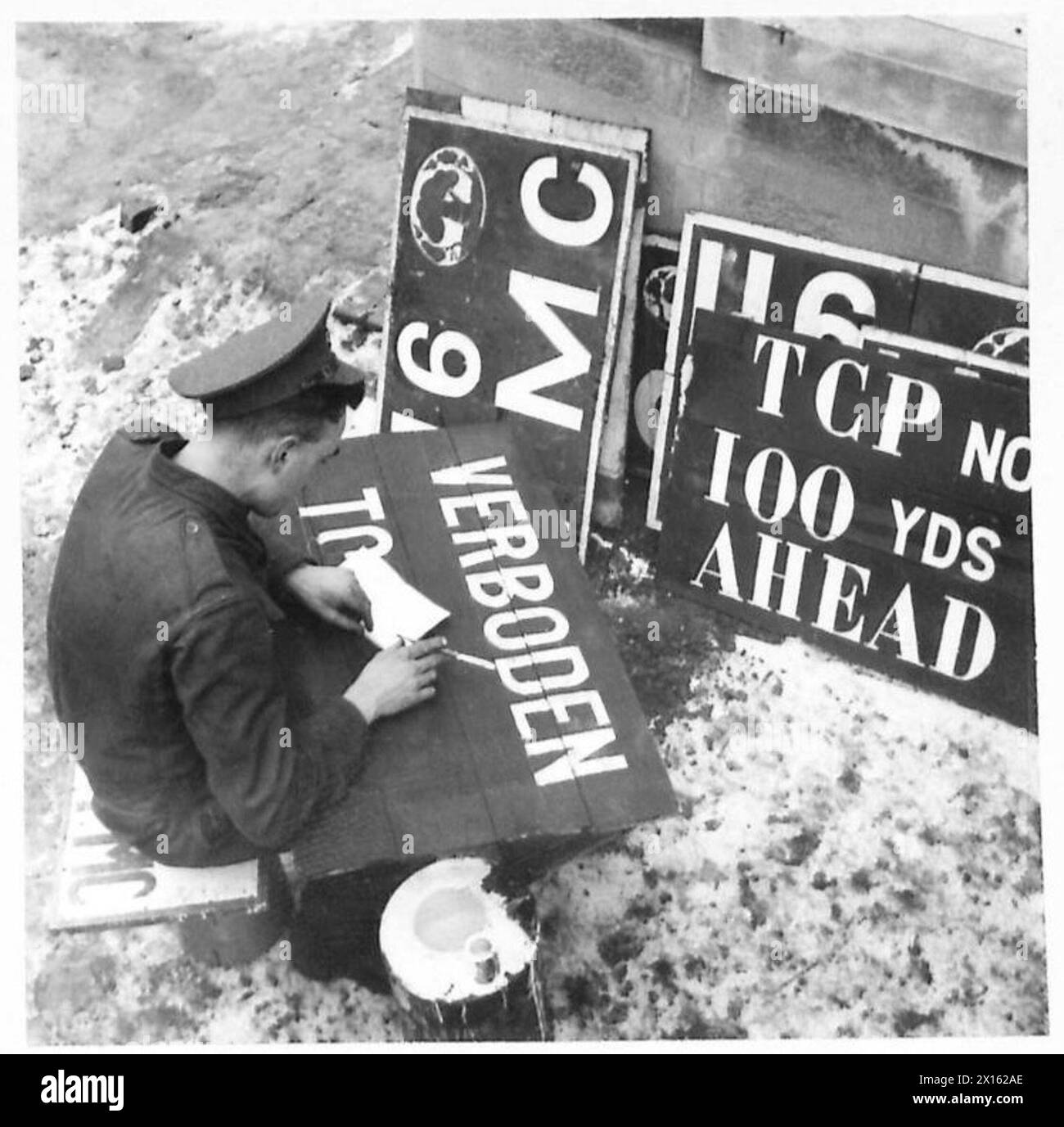 Il caporale di Lance H.A. Kerr dello Stein Corps of Military Police dipinge un cartello "Don't Enter" mentre fa riferimento a un dizionario, in servizio presso il British Army, 21st Army Group. Foto Stock