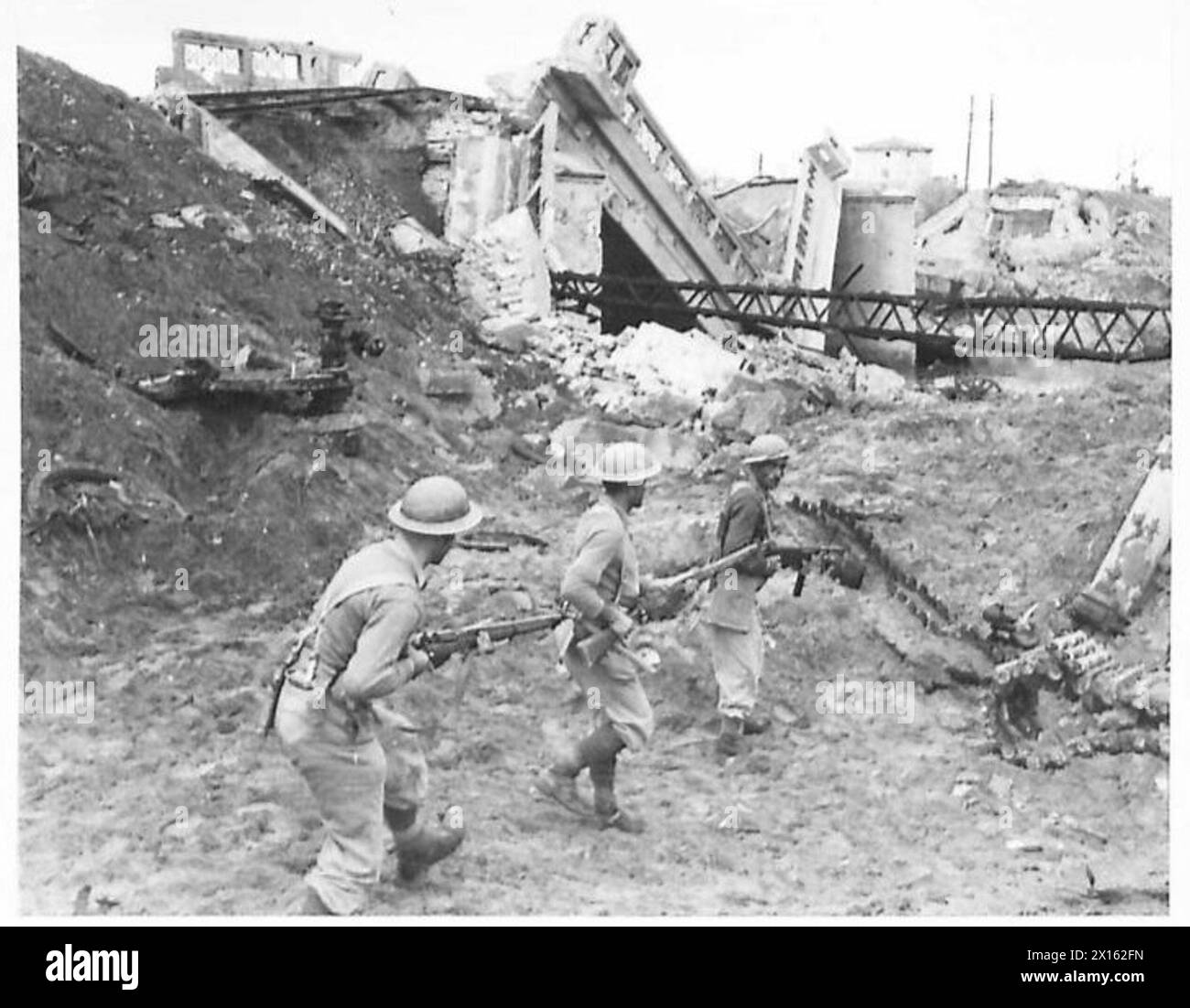 La fanteria greca pattuglia le rive del fiume vicino a un ponte ferroviario soffiato, con i resti di un carro armato nemico distrutto da una bomba visibile, operazioni dell'esercito britannico. Foto Stock