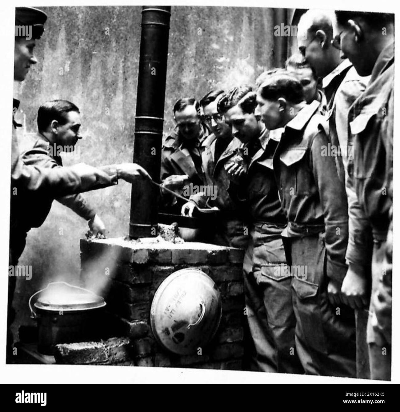 Gli ufficiali imparano le tecniche di cucina sul campo utilizzando forni improvvisati, guidati dal comandante della scuola, sottolineando il lavoro pratico e l'iniziativa. Foto Stock