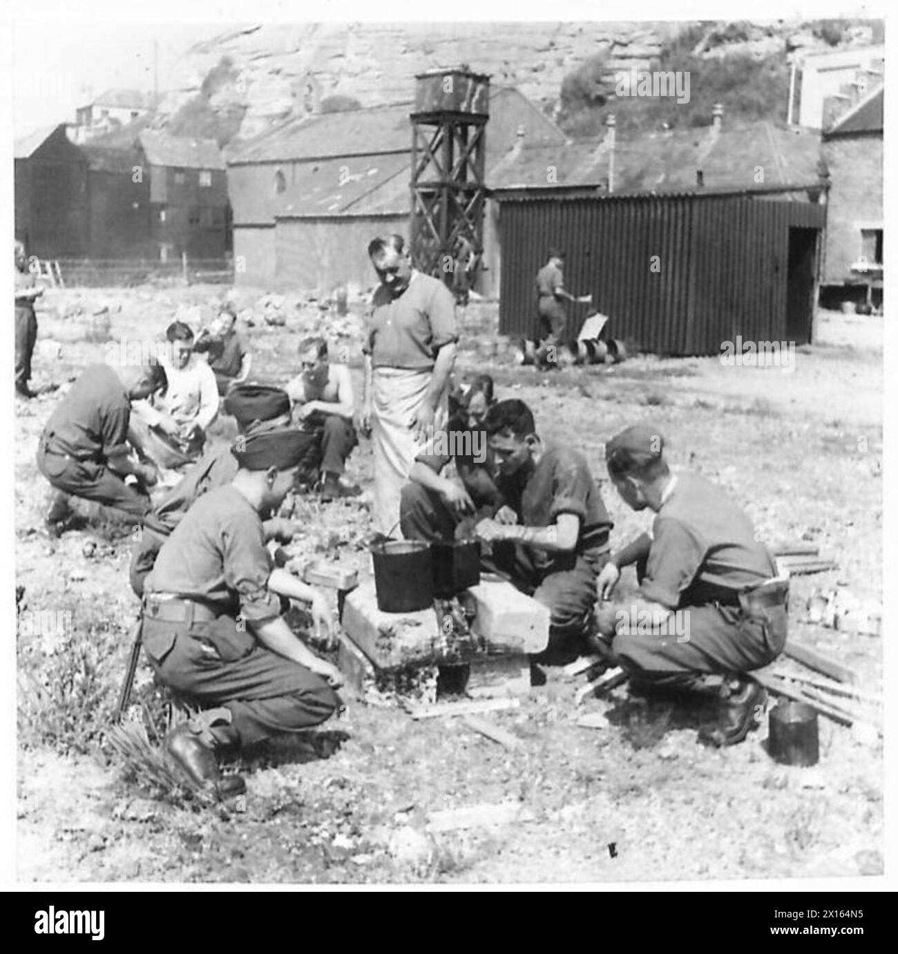 Il personale di una batteria di difesa costiera prepara le proprie razioni su incendi improvvisati durante una giornata senza cuocere. Foto Stock