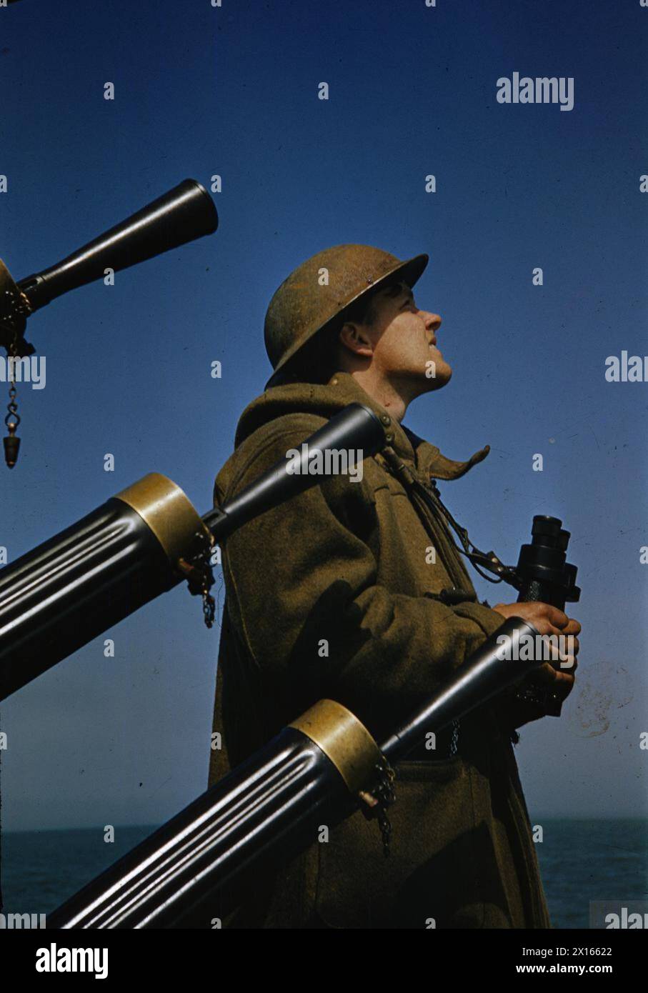 Un marinaio della Royal Navy di guardia nel 1942 indossa un mantello e un casco in acciaio mentre tiene un binocolo accanto a un quadruplo cannone antiaereo Vickers da 0,5 pollici durante la seconda guerra mondiale Foto Stock