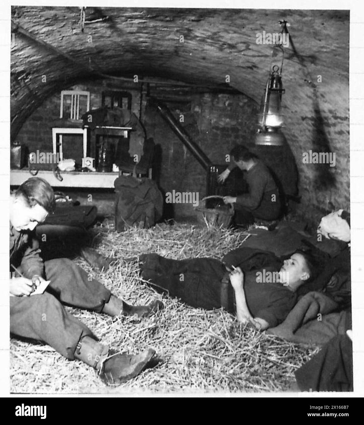 I soldati dell'esercito britannico del 21st Army Group riposano e dormono in una cantina utilizzata come billette nelle aree occupate dai tedeschi, usando scatole di munizioni come incendi. Foto Stock