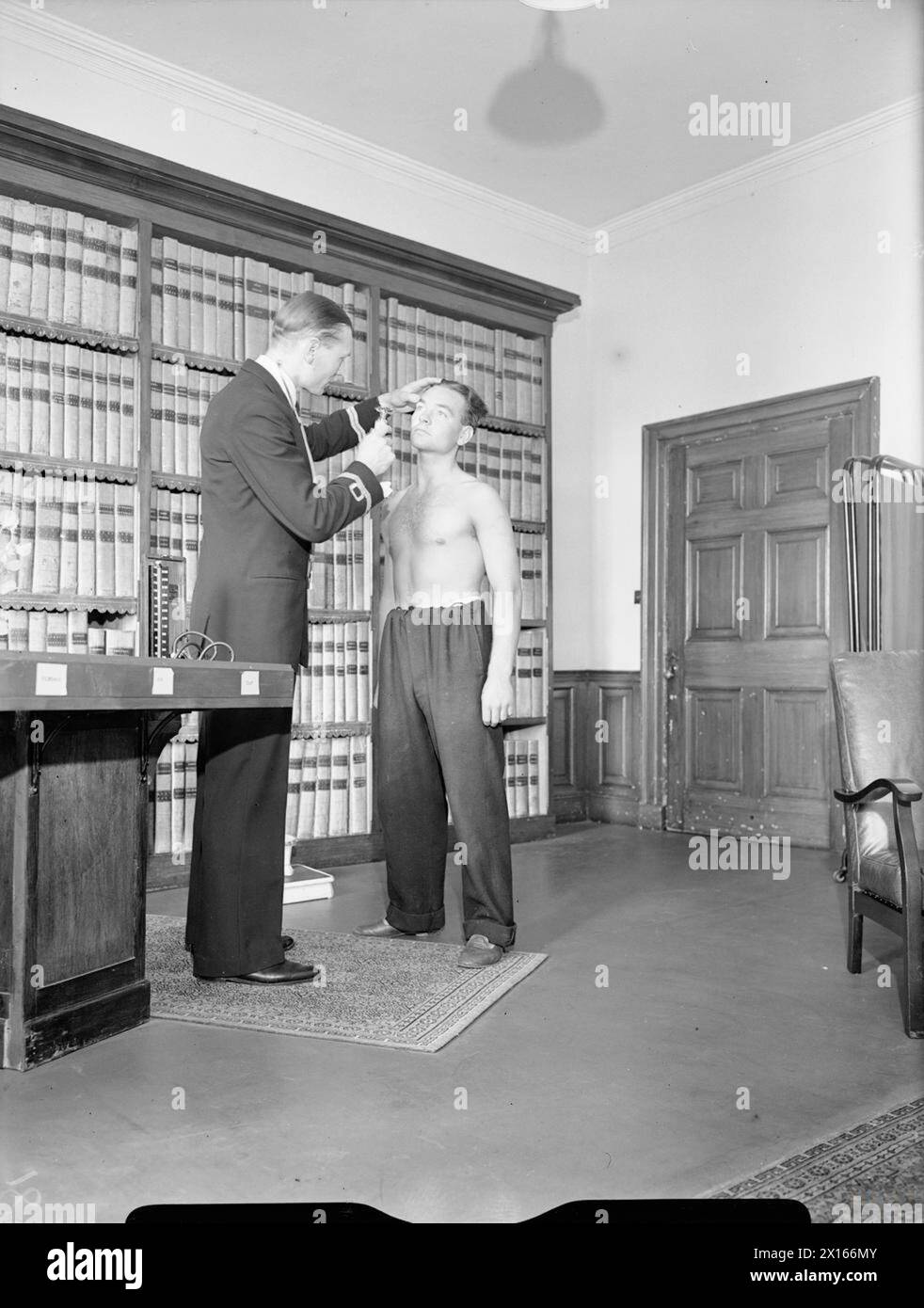 Cholmondeley Castle nel Cheshire è stato un ospedale ausiliario della Royal Navy durante la seconda guerra mondiale. Un paziente sta facendo un esame oculistico in una piccola biblioteca mentre i libri rimangono sugli scaffali. Foto Stock