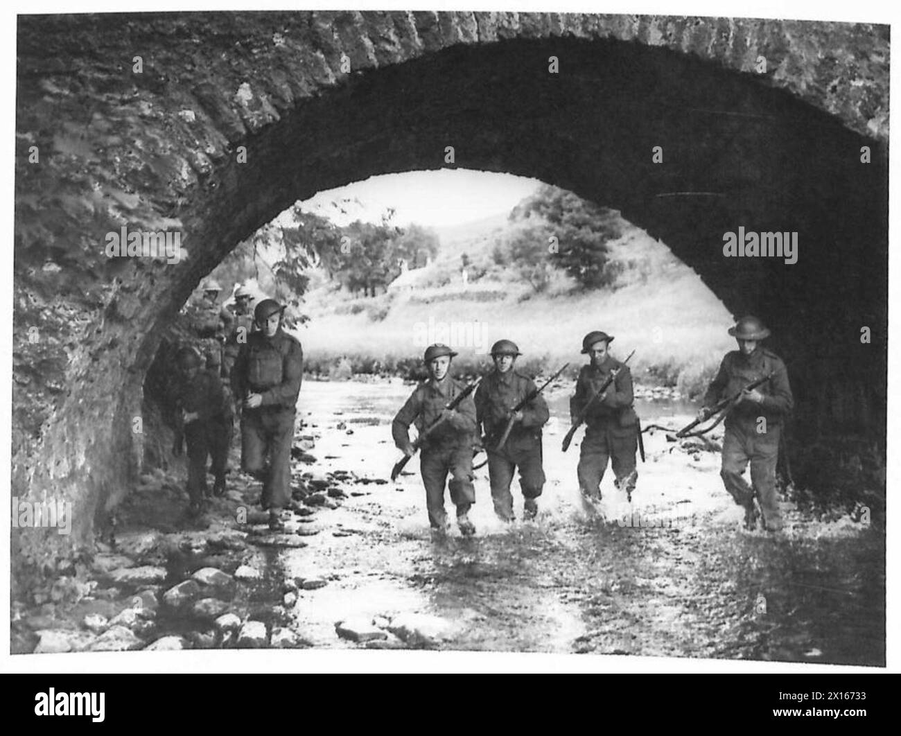 Una pattuglia dell'esercito britannico manovra attraverso l'acqua sotto un ponte durante un'esercitazione di confine. Foto Stock