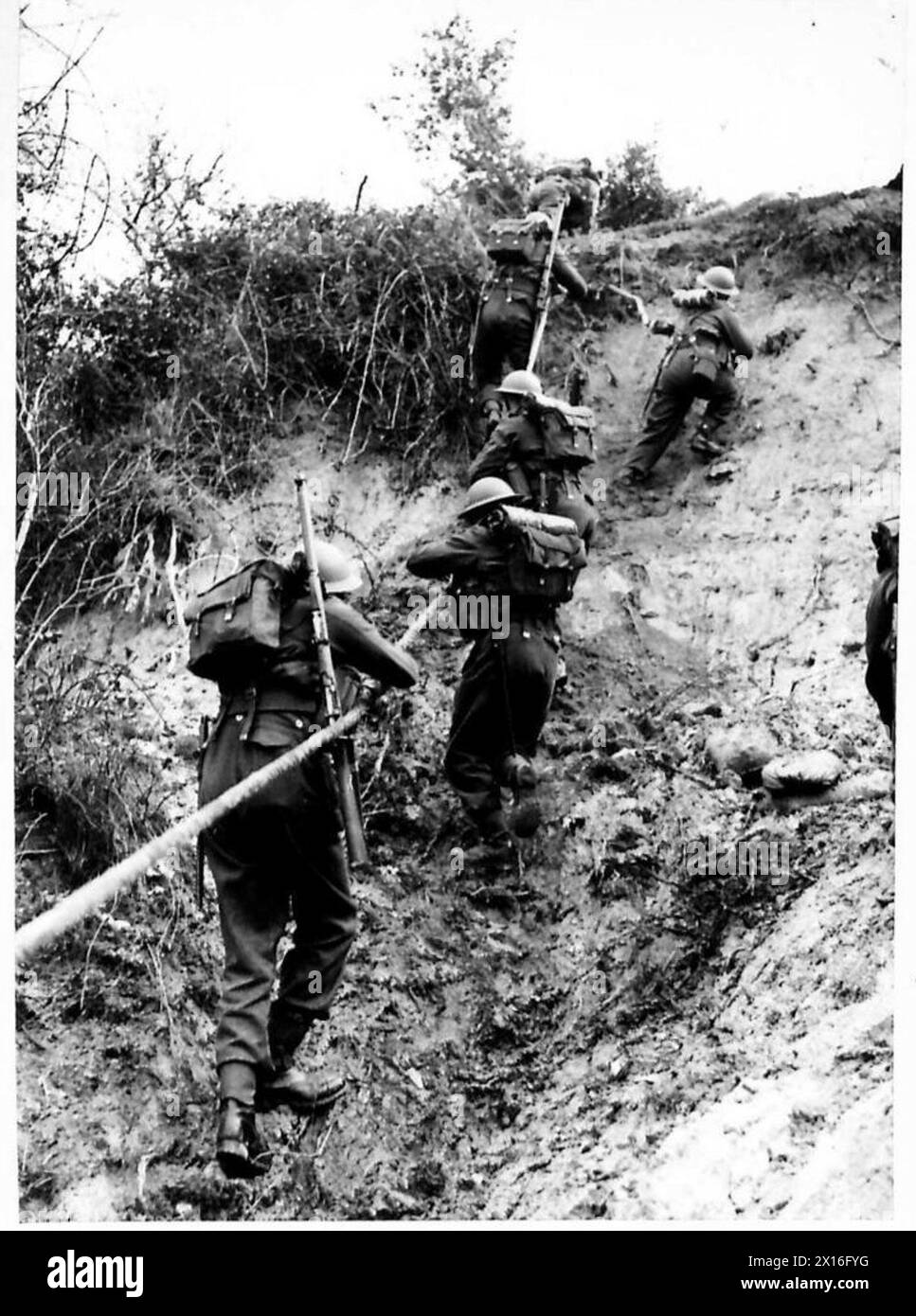 Un battaglione del Suffolk Regiment conduce un faticoso esercizio di addestramento offensivo, scalando le scogliere mentre trasporta attrezzature da combattimento complete, sottolineando la resistenza fisica e la preparazione tattica. Foto Stock