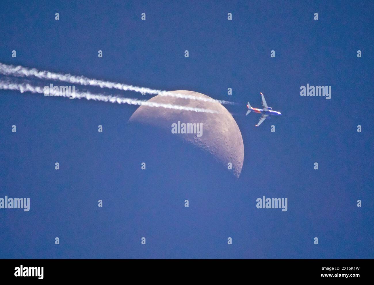 Un aereo di linea commerciale ad alta quota con contraglie vola oltre una luna crescente in un cielo blu profondo. Foto Stock