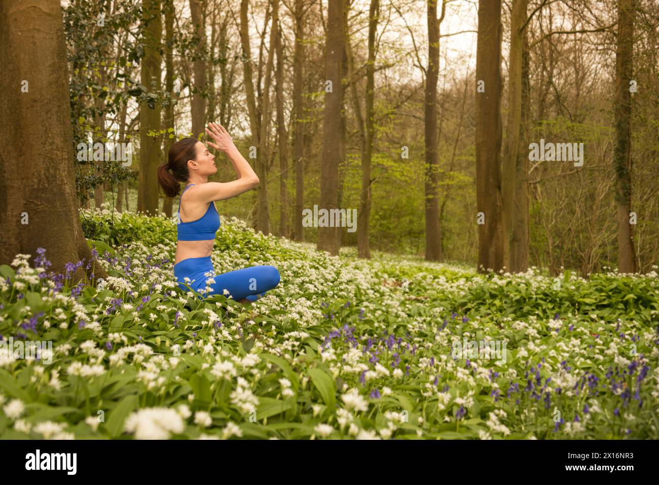 donna che medita in natura, aglio selvatico, prato e foresta bluebell. Fitness in primavera e estate. Foto Stock