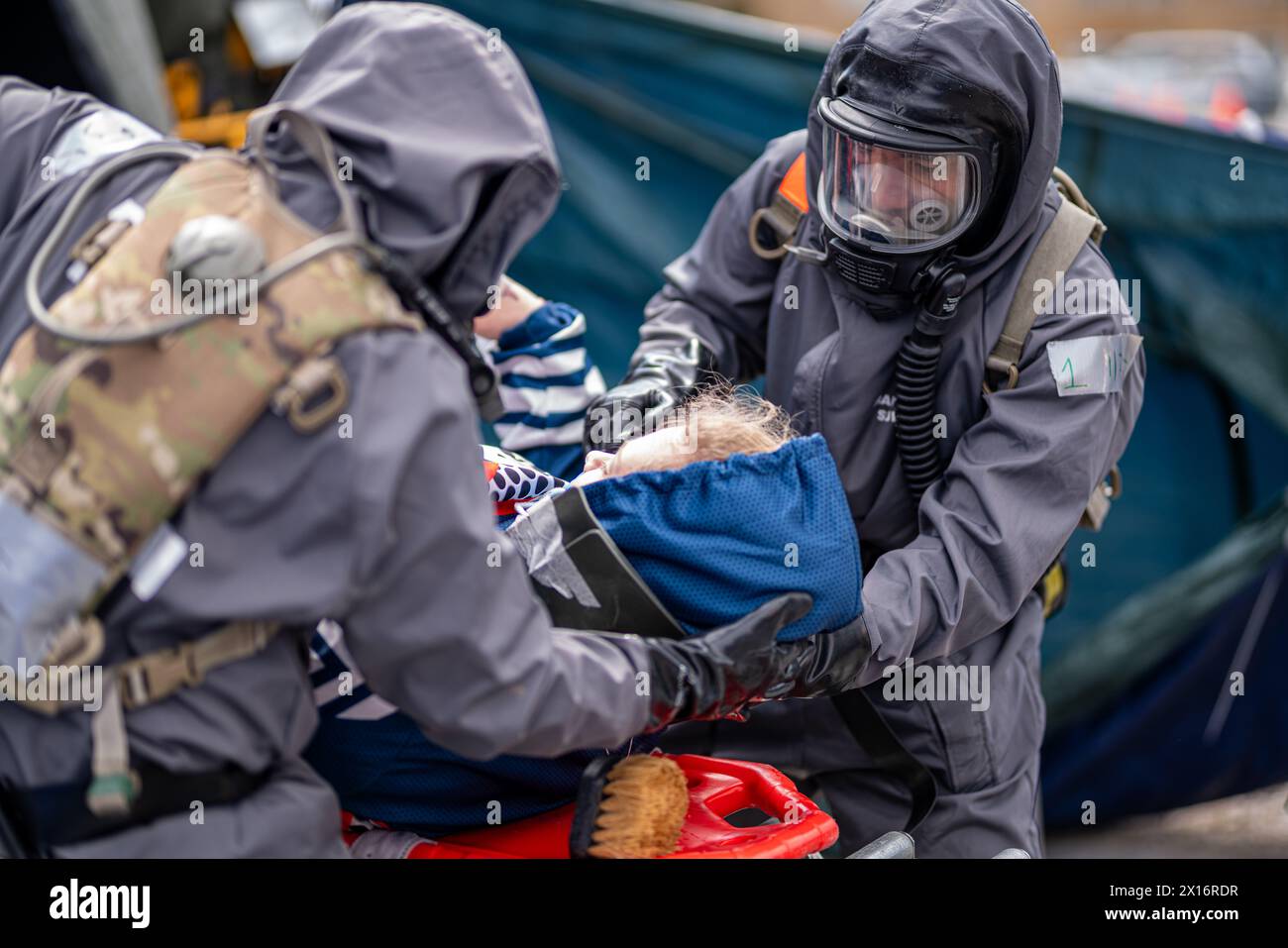Un uomo con una tuta hazmat sta aiutando un bambino. La scena è tesa e seria, poiché l'uomo indossa una maschera antigas e il bambino viene trattenuto Foto Stock