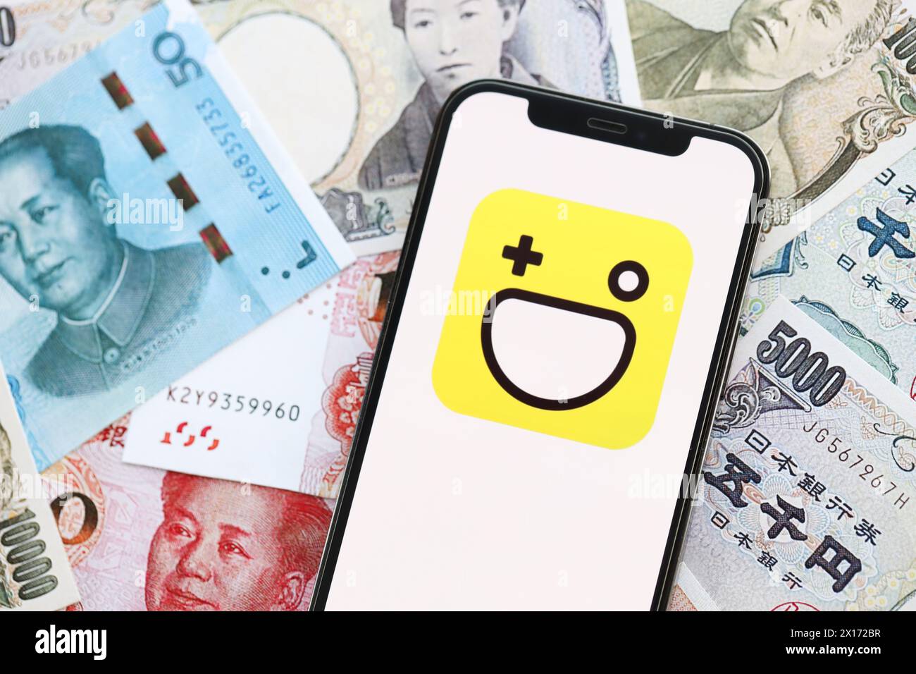 KIEV, UCRAINA - 1 APRILE 2024 icona Hago sullo schermo dello smartphone su molte banconote asiatiche. Display iPhone con logo app con banconote in yen giapponesi e yuan cinesi Foto Stock