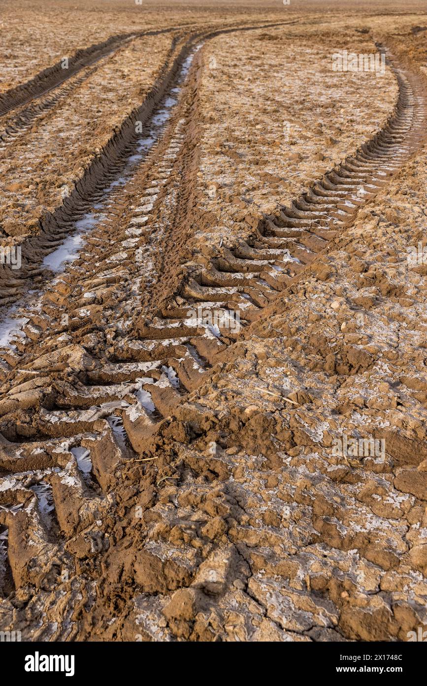 un tracciato profondo di un'auto pesante in un campo, un campo arato con terreno ghiacciato e tracce di macchinari agricoli Foto Stock