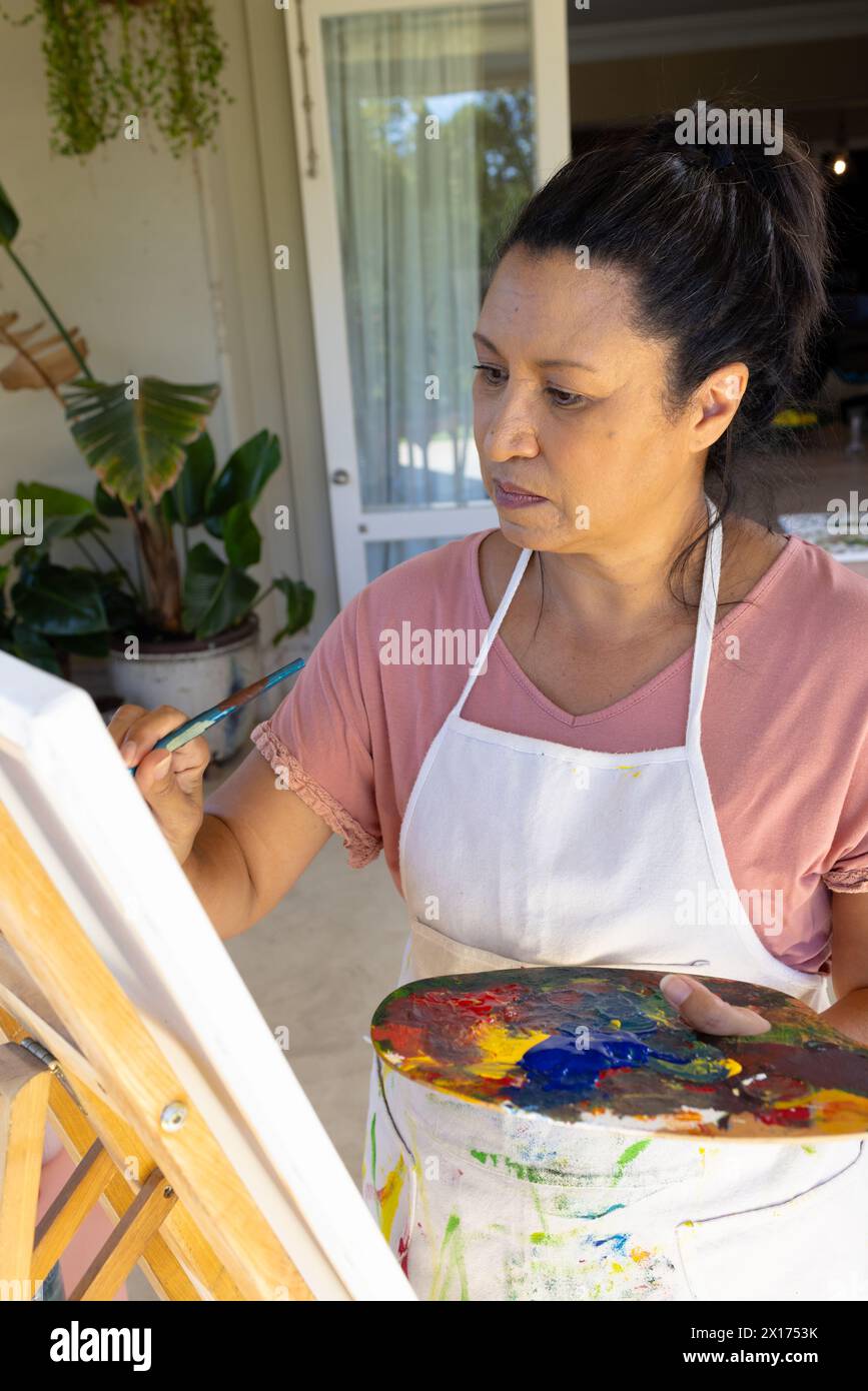 Donna birazziale matura che dipinge su tela a casa, concentrata Foto Stock