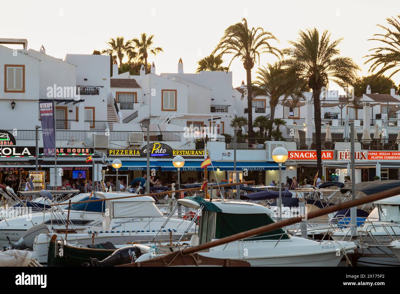 I turisti passeggiano davanti agli accoglienti ristoranti, bar e ristoranti lungo il porto di Cala en Bosch op Menorca. Foto Stock
