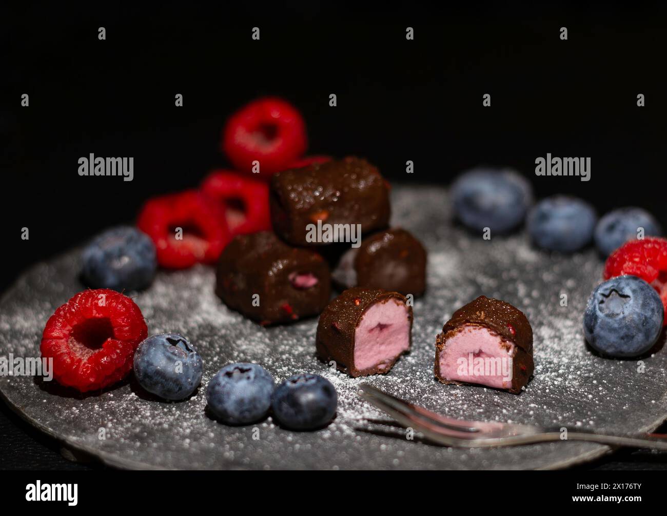 Bocconcini di gelato di frutti di bosco misti al cioccolato con lamponi e mirtilli su un piatto di ardesia Foto Stock