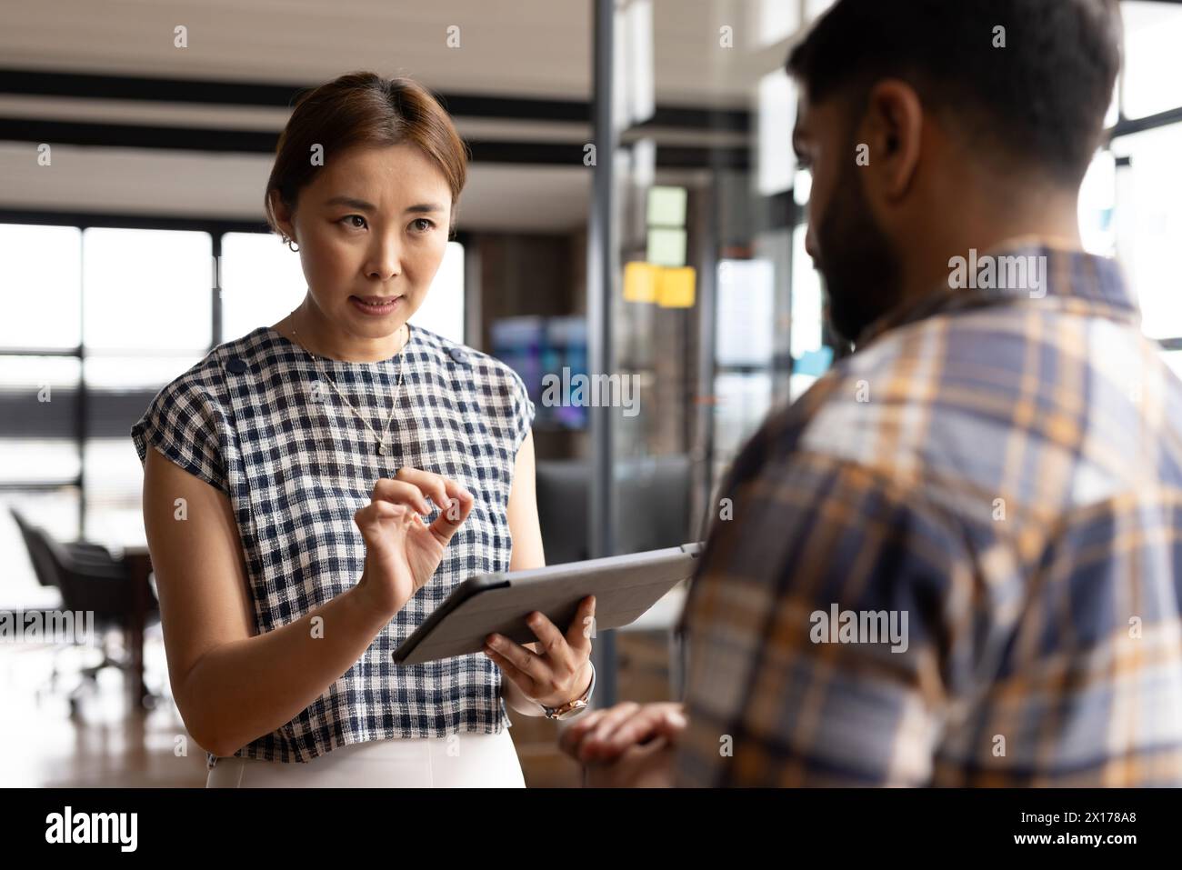 Donna asiatica di mezza età che mostra tablet a un giovane uomo asiatico in un moderno ufficio aziendale Foto Stock