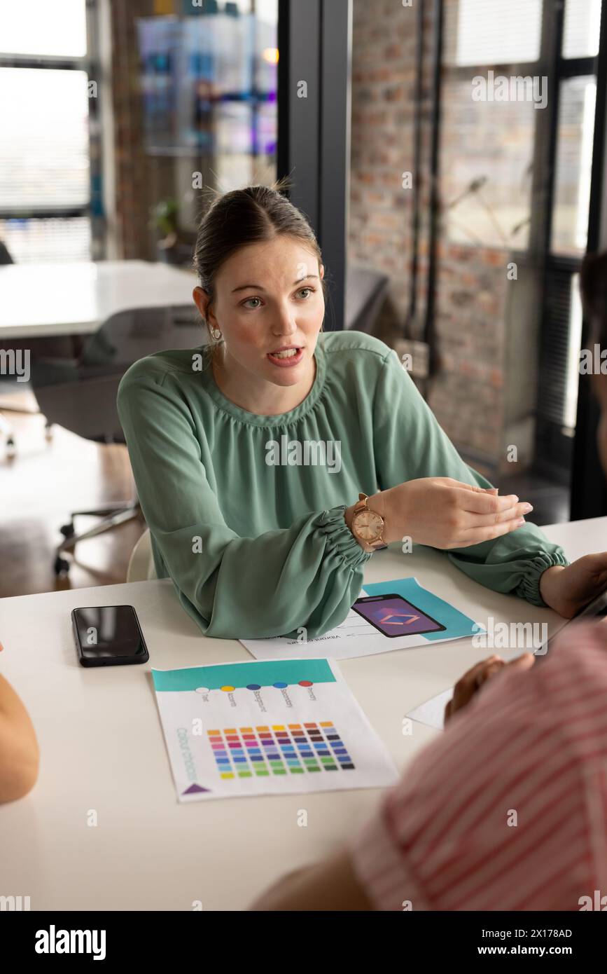 Giovane donna professionista caucasica in camicetta verde parla con i colleghi in un moderno ufficio aziendale Foto Stock