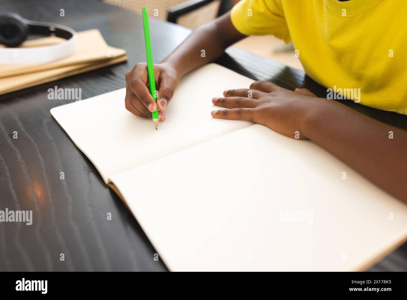 Ragazzo afroamericano che disegna con un quaderno, indossa una camicia gialla Foto Stock