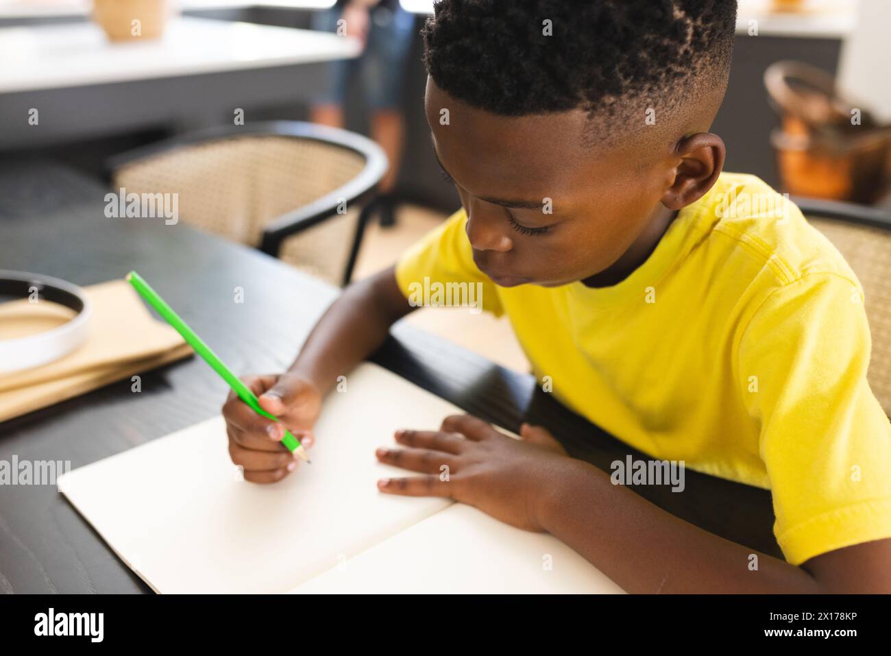 Ragazzo afroamericano che disegna a tavola, concentrato sulla carta Foto Stock