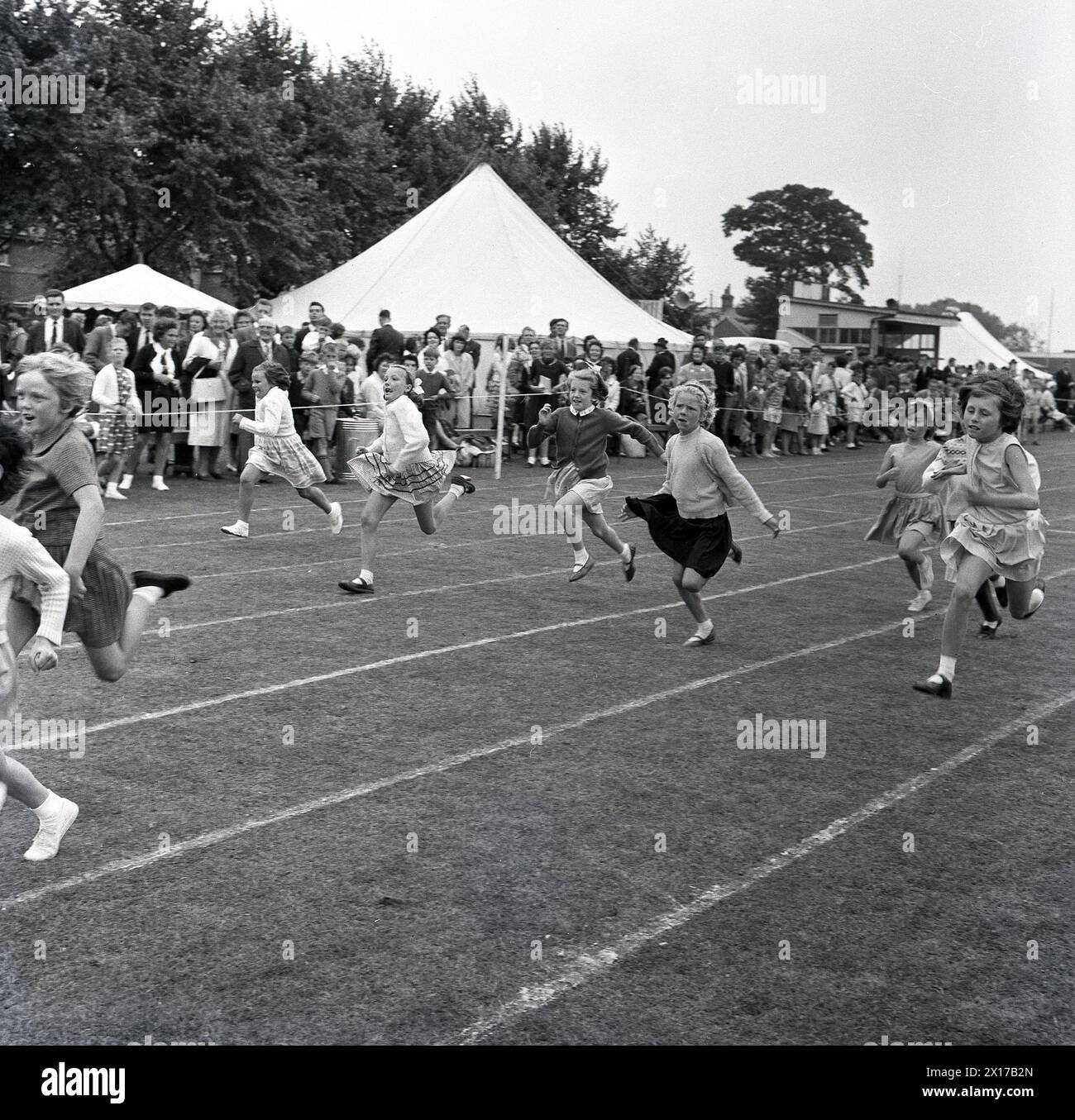 1964 ragazze storiche che partecipano a una gara di corsa su una pista erbosa in una giornata di sport e attività locali. Foto Stock